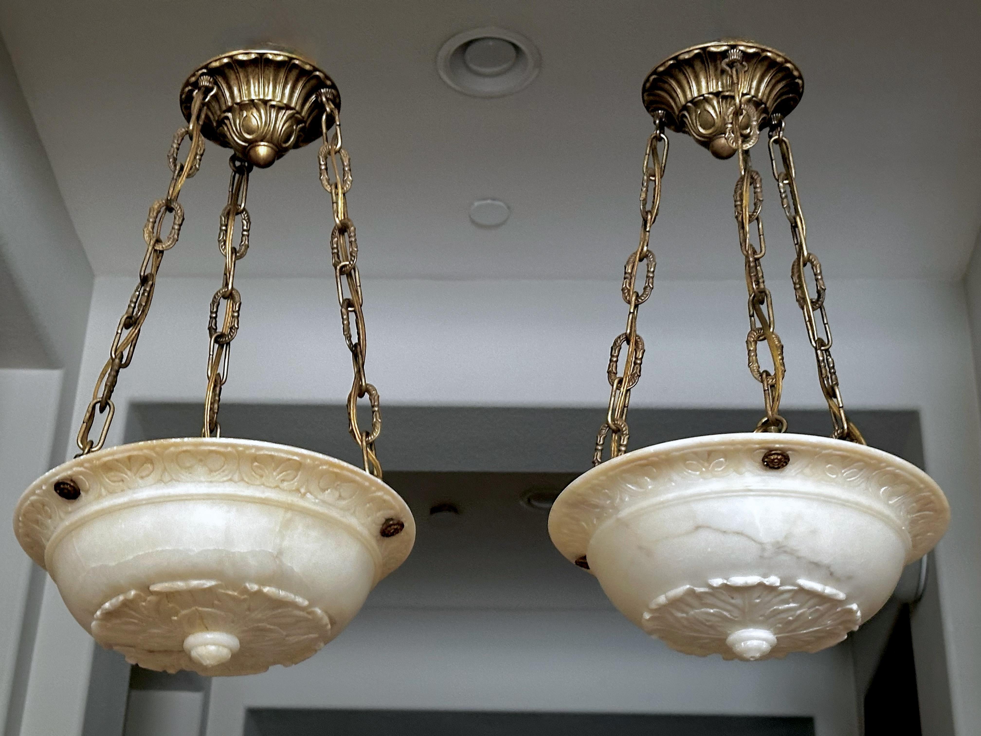 Pair of smaller scale finely carved Neoclassic style alabaster chandelier pendant ceiling lights, with all new aged patinated brass fittings, chain and ceiling canopy. The intricately carved alabaster bowls are attributed to EF Caldwell. Each newly