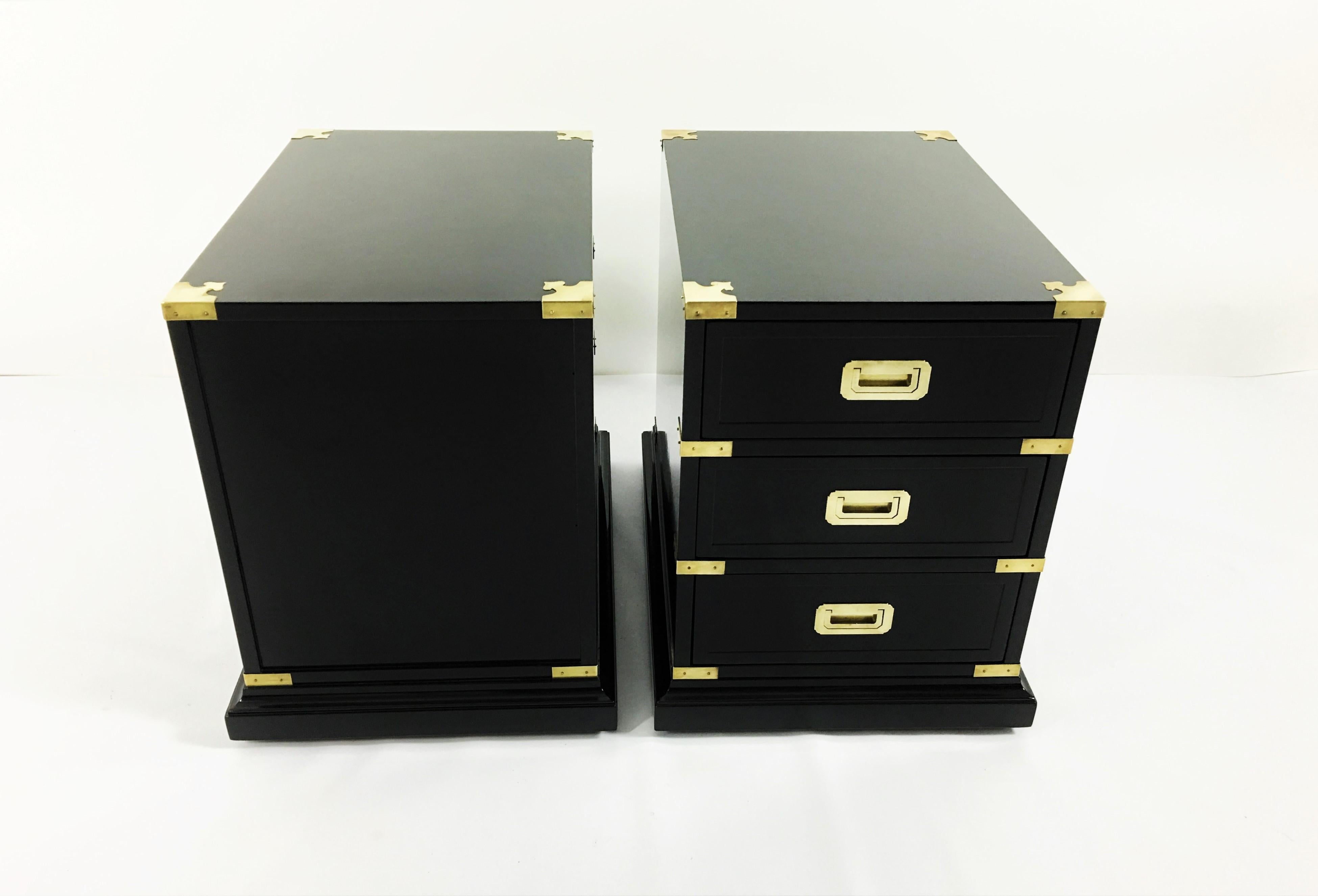 Elegant pair of black lacquered Campaign style side tables manufactured by Hekman Furniture, circa 1930s. Richly adorned with gilt brass hardware and trim details, dovetailed drawers and on wheels. Finished on all sides.