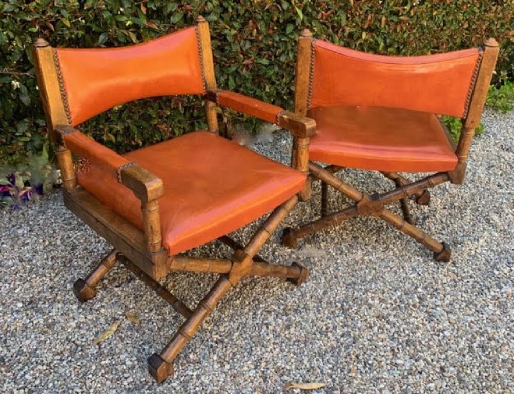 A wonderful pair of wood and orange leather campaign style chairs. The fabric is original and does have some wear, but overall is wonderfully patinated with a worn in look. The wood frames are very sturdy and perfectly suited for any den or living