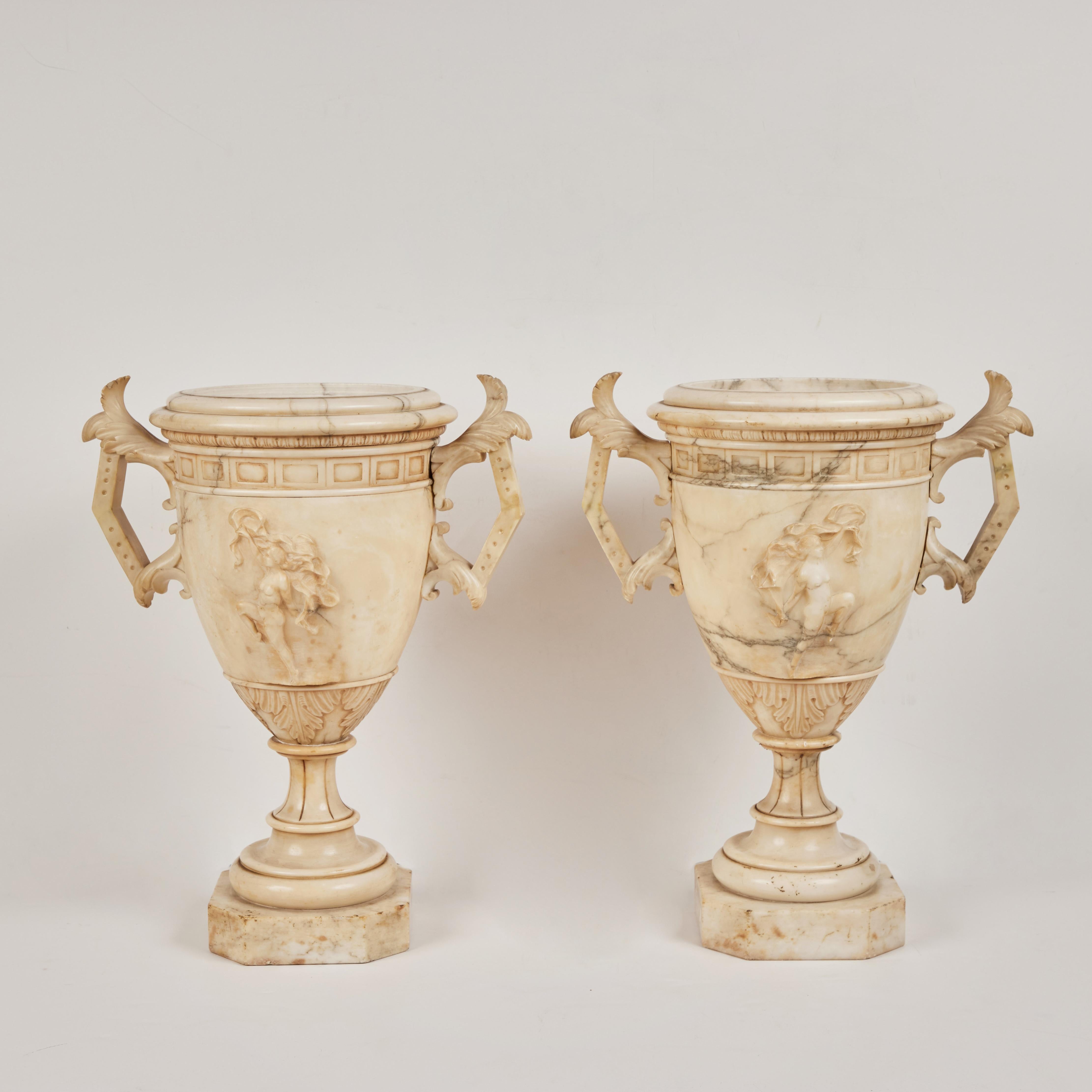 An impressive pair of hand carved, lidded alabaster urns with left and right reliefs of a female mythological figures and Greek key design. Each, 3 separate pieces, base, center and lid. From the area of Florence, Italy.