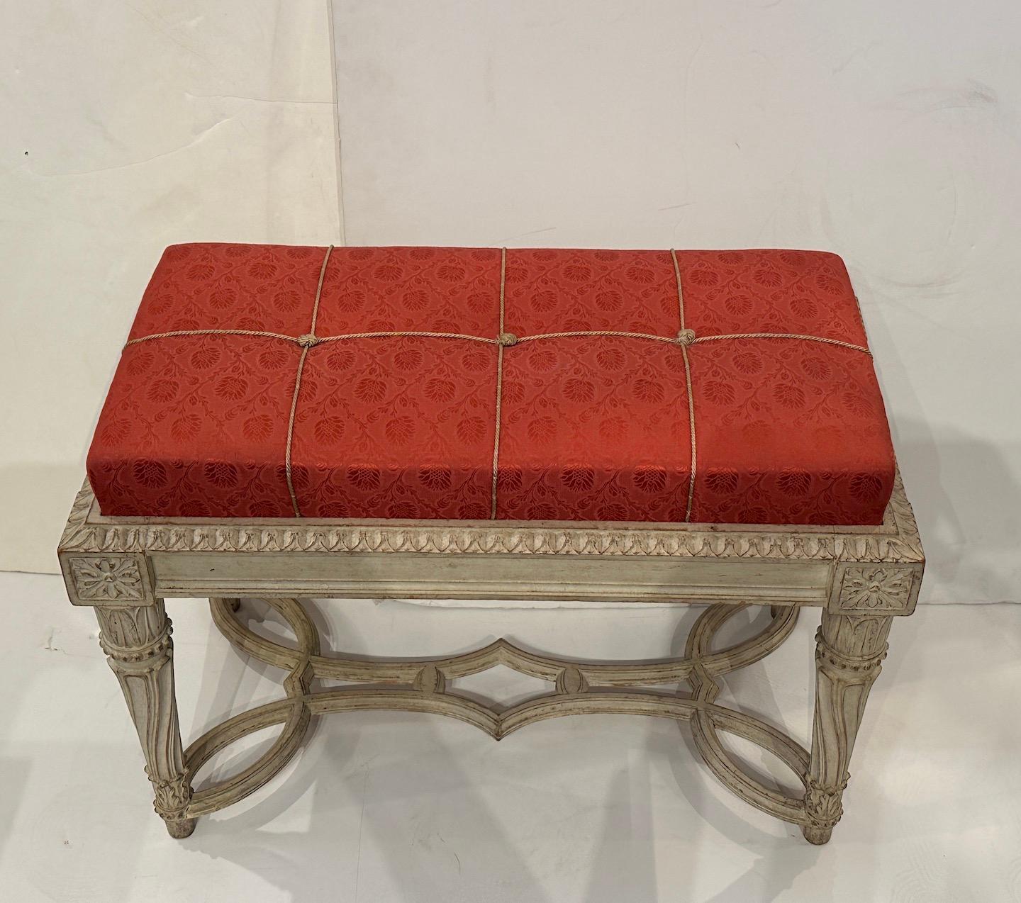 A chic pair of hand carved, white gessoed with wax finish benches, circa 1900.  Elaborate stretchers.  More recently upholstery in a beautiful damask fabric in red tones, finished with tied and knotted trim. 