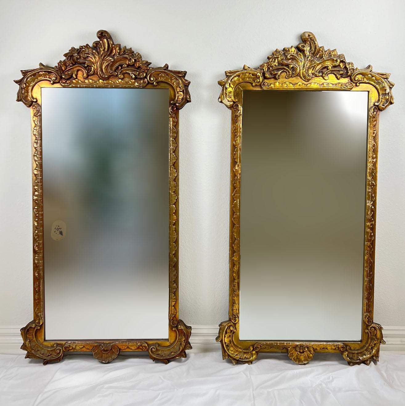 Une paire de miroirs dorés anciens encadrés de bois avec une touche d'élégance classique. Ces miroirs présentent des cadres dorés ornés qui témoignent d'un travail artisanal complexe. Si les miroirs eux-mêmes présentent quelques taches et les cadres