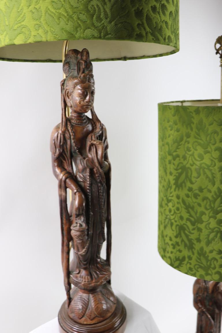 Very stylish and chic pair of carved wood Tibetan Buddha table lamps, complete with original decorative shades. 55 in Total H x 29 in H of Buddha figure x Shade 21 in H x 17 in Dia. x 7 in. Dia. of Base. Offered and priced as a pair.