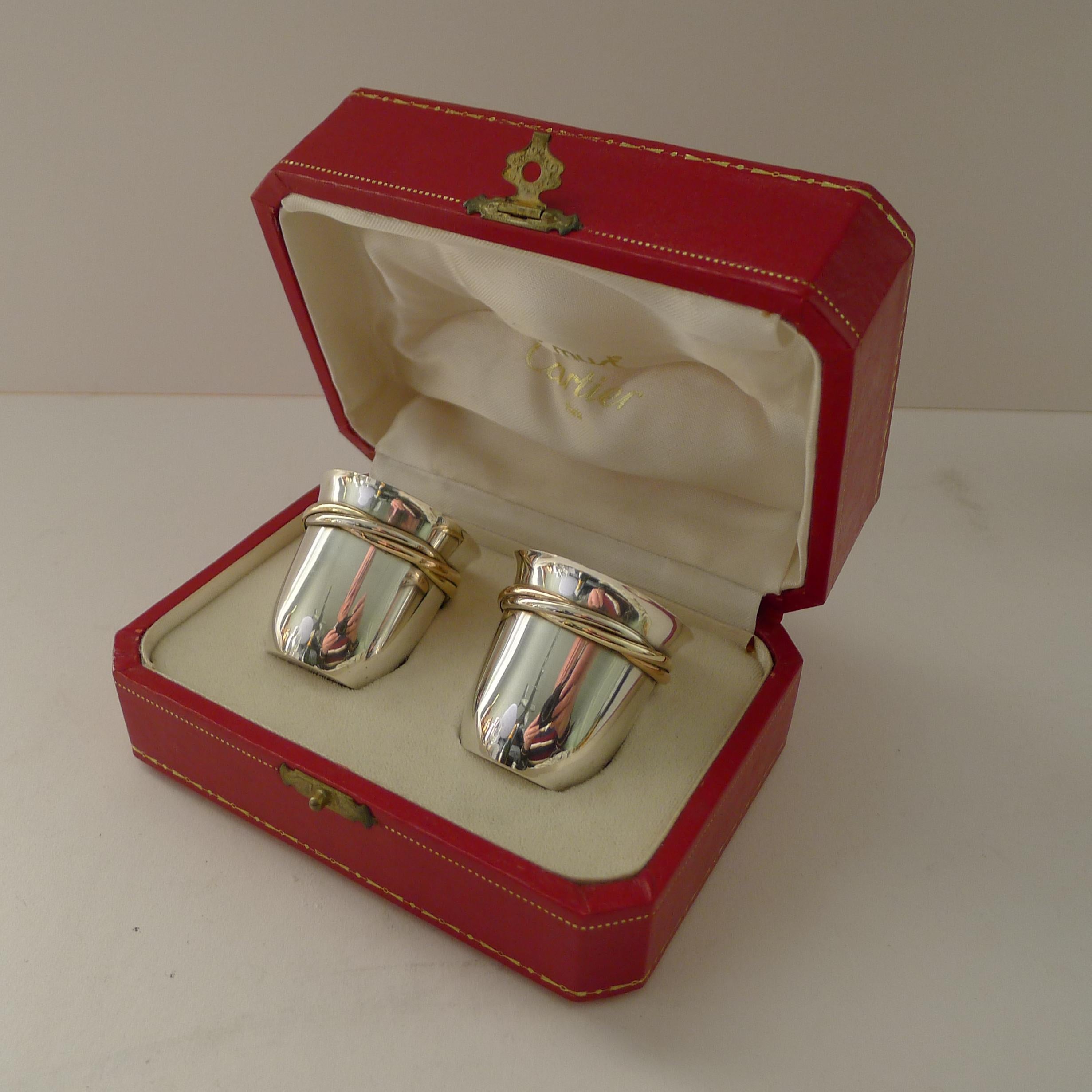 A wonderful pair of French solid / sterling silver shot cups with the three colour gold (plated) bands around the top of each; the Trinity design.

Both look to be unused complete in their original Must de Cartier presentation box from a jewellers