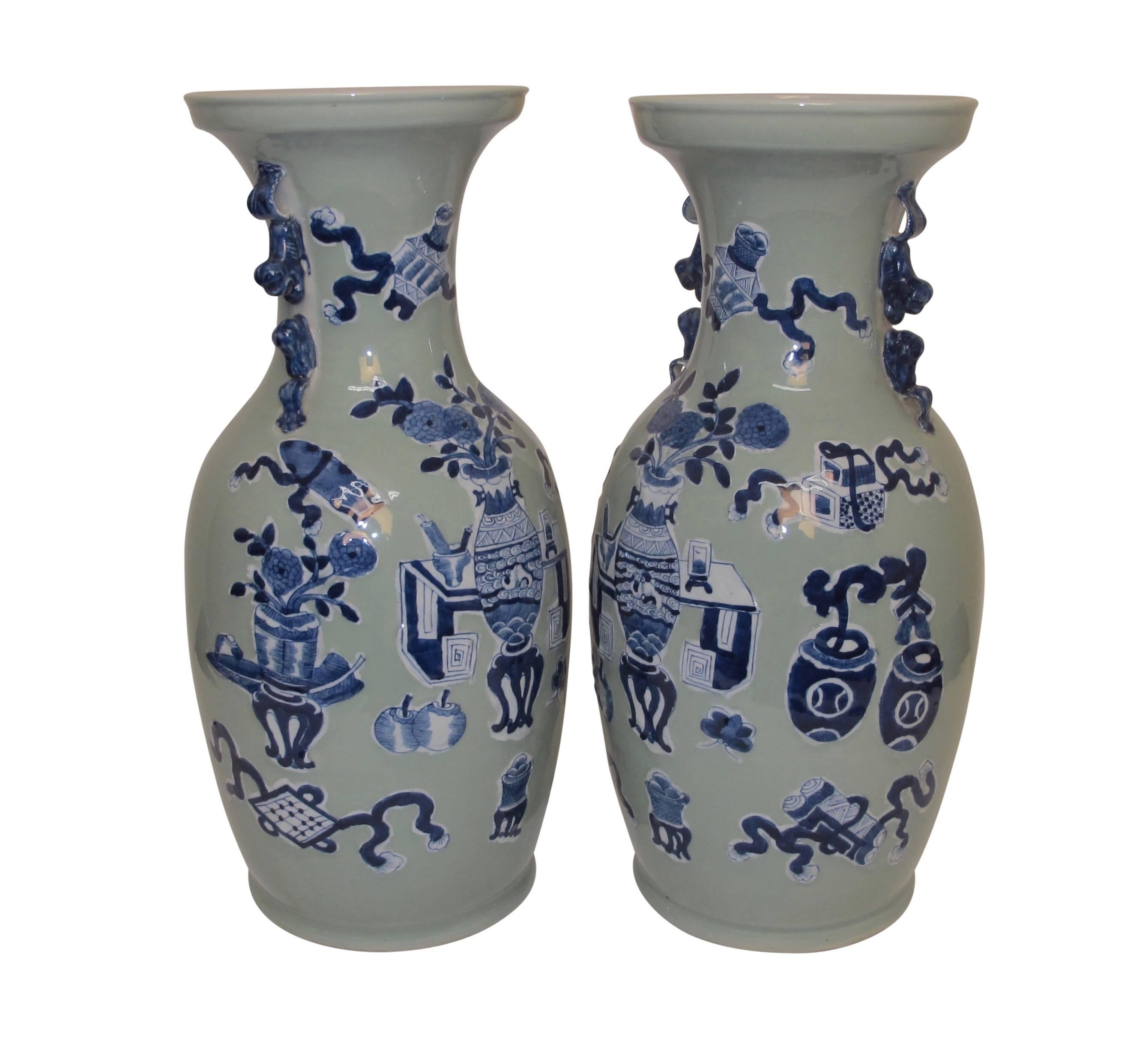 Pair of tall and handsome celadon vases with two pair of crouching lions on each side of the neck, and having various scholar symbols among vases of flowers and pots of flowering plants and fruits, Chinese, late 19th century.
