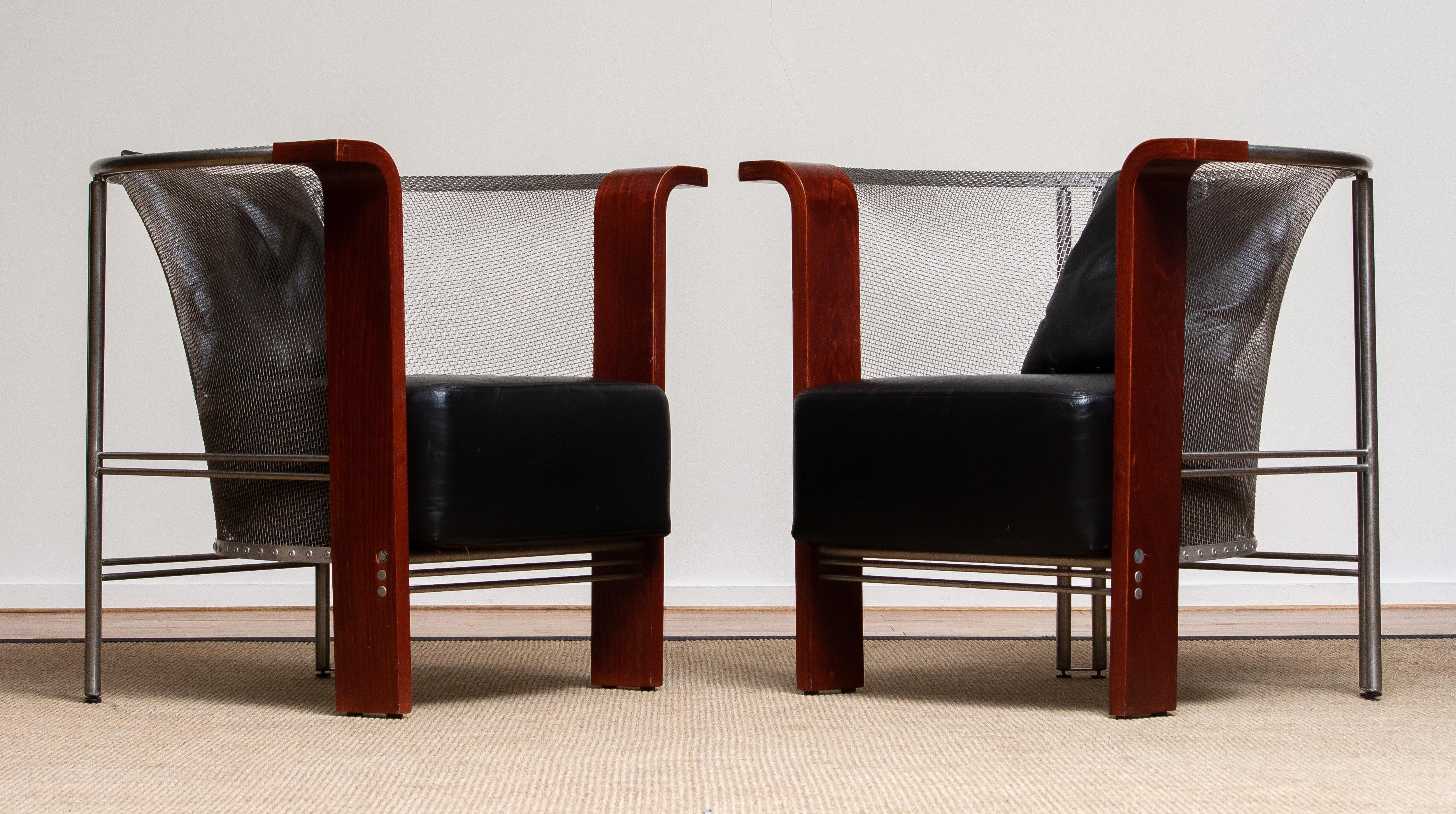 Extremely beautiful and architectural set of two Post Moderen style club / lounge / easy chairs made of stainless steel mesh and welded stainless steel in combination with black leather and bended plywood, mahogany color. 
These chairs are designed