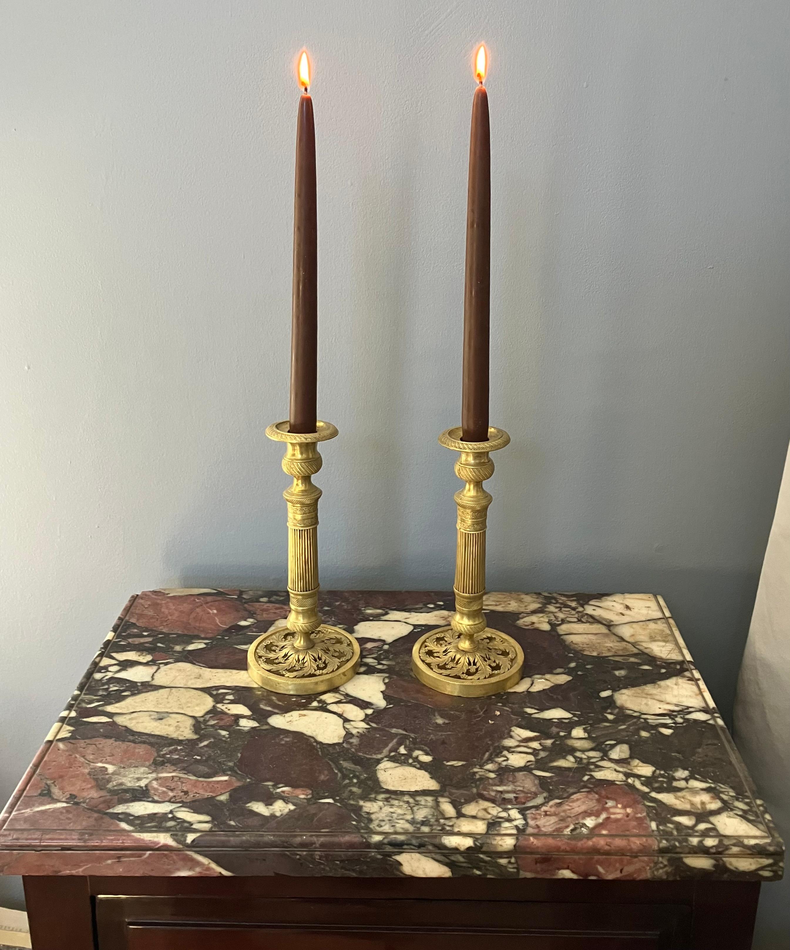 Coppia di candelieri in ormolu Charles X.  Coppia di candelieri francesi in stile florido neoclassico con fusto scanalato, bobeche perlinate e capitelli con fascia floreale e arabescata e abbellimento a fogliame aperto; con elementi in ottone e