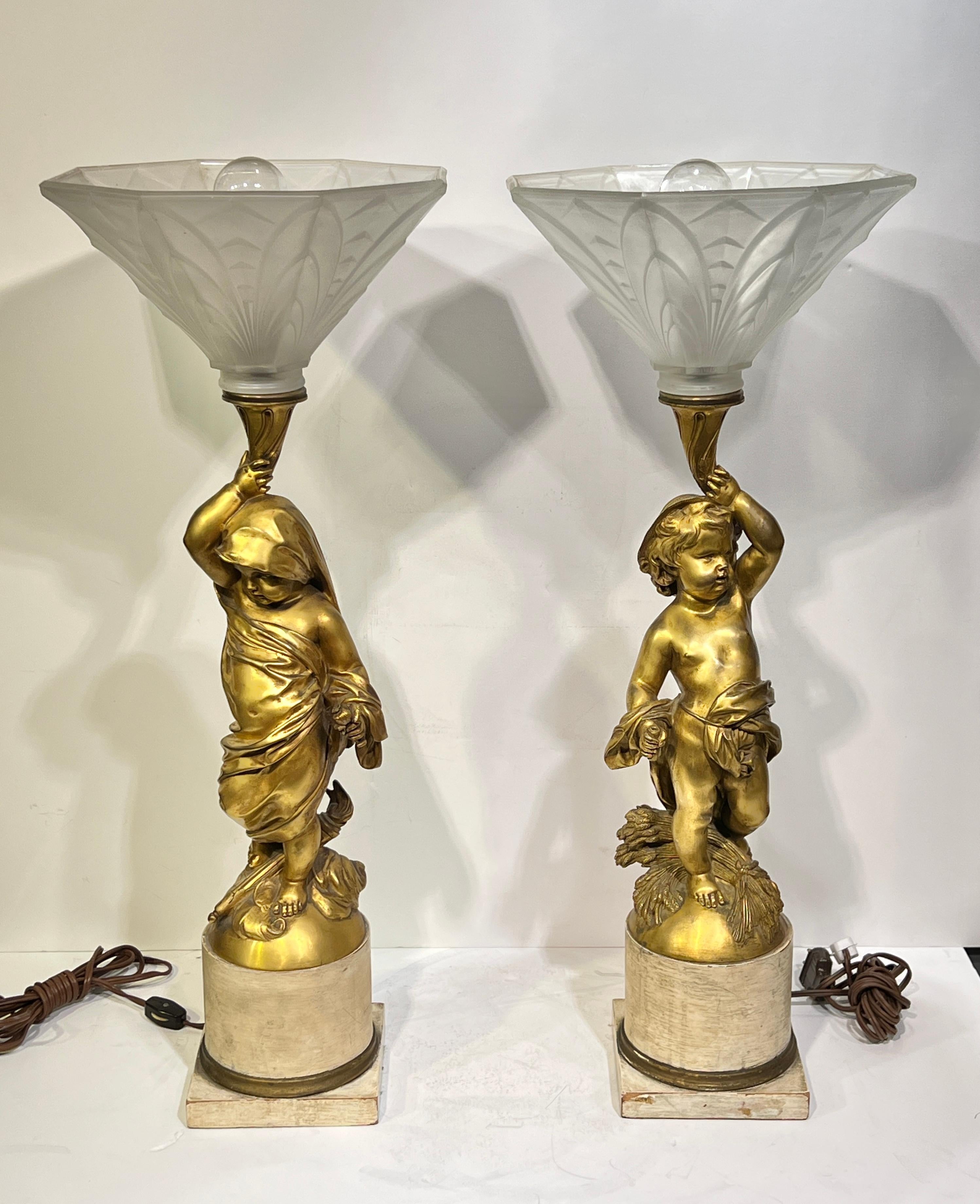 Pair of antique (late 19th to early 20th century gilt bronze figures of putti supporting octagonal shape frosted glass shades, mounted on wooden plinths.  Each 25.75 inches tall and the shades 9.75 inches wide/deep.  With modern wiring, ready for