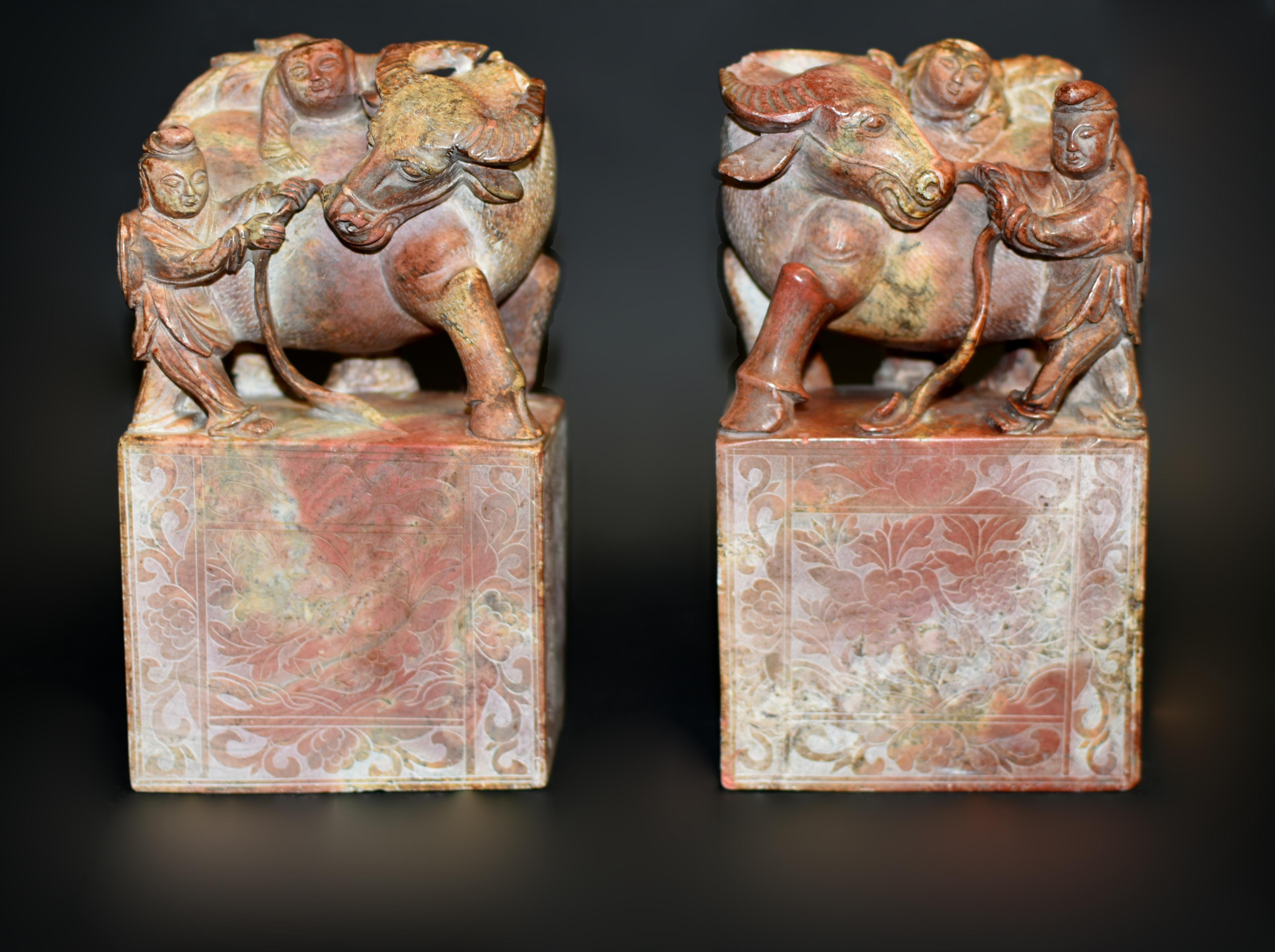 Cette grande et remarquable paire de statues/ serre-livres en pierre massive témoigne d'un travail artisanal et artistique magistral, chaque pièce étant méticuleusement sculptée. La partie supérieure présente une scène pastorale vivante : un buffle
