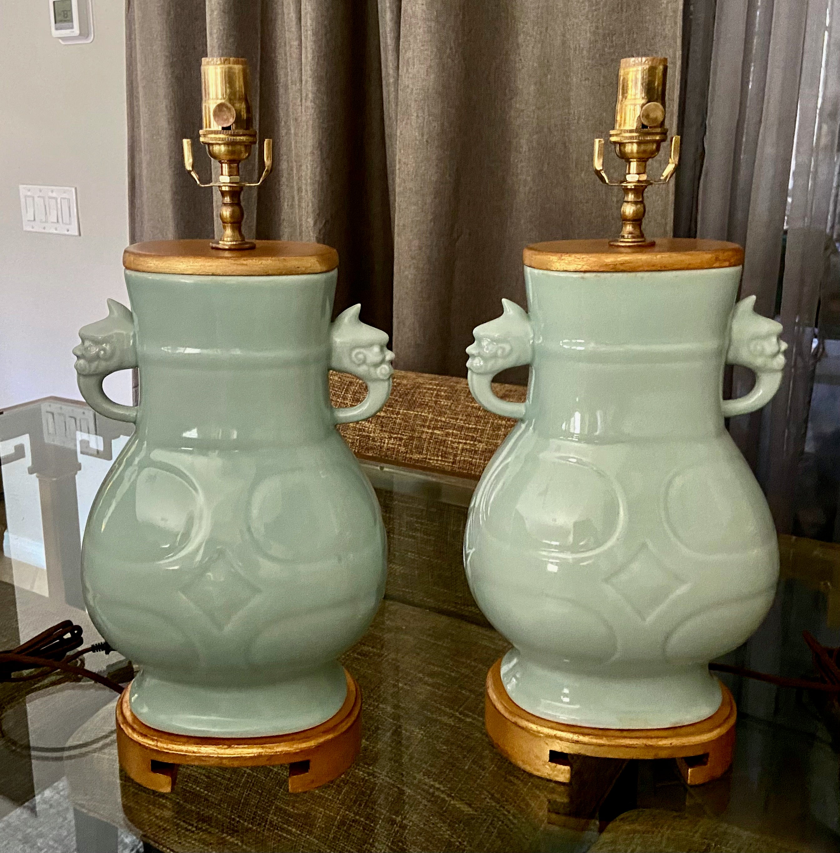 Pair of Chinese Asian celadon green porcelain table lamps with warrior face handles. Each mounted on giltwood bases along with matching vase cap. Newly wired with new 3 way brass sockets and rayon cords. The rectangular shape measures 21