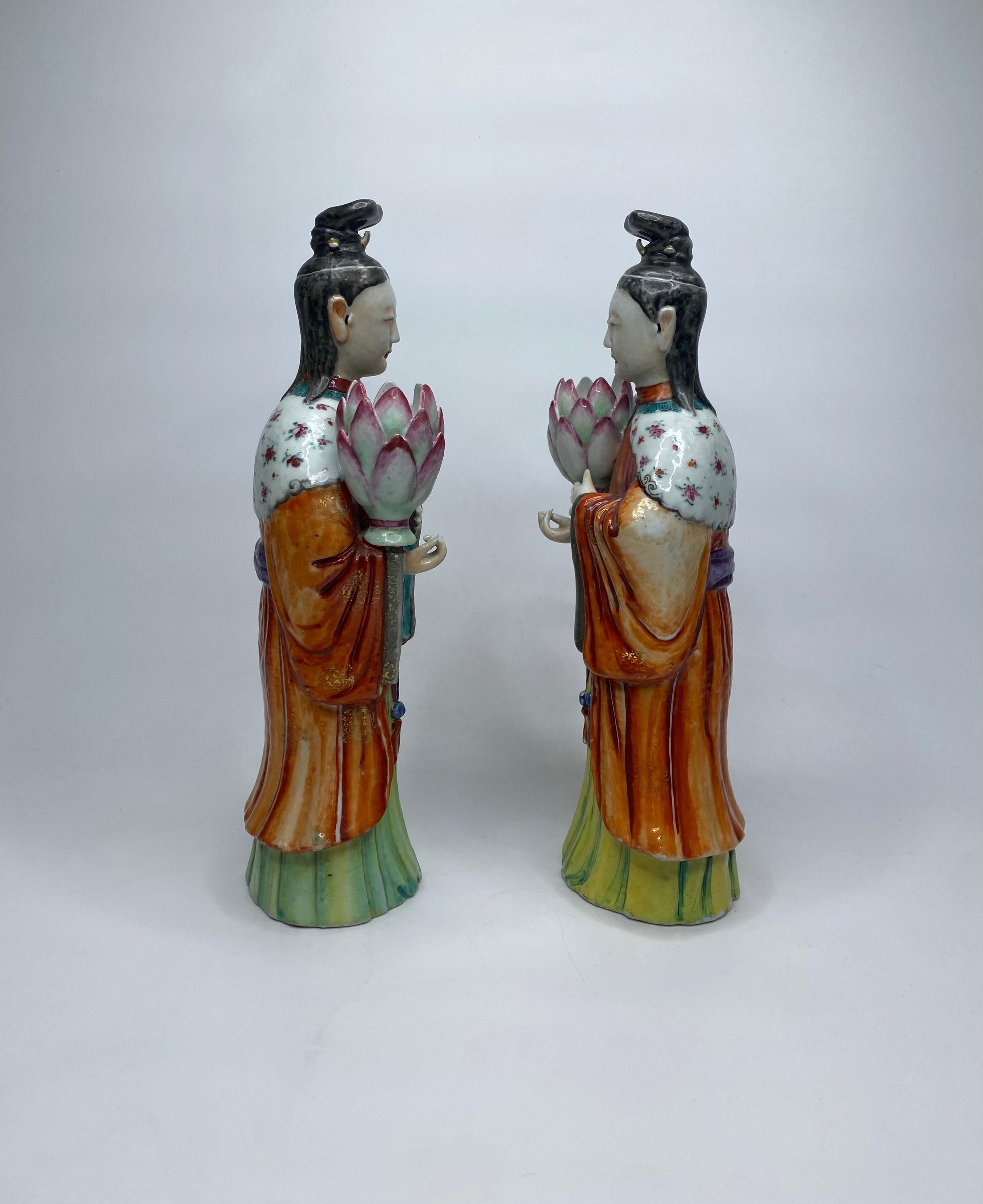Paire de chandeliers en porcelaine de Chine, vers 1760, période Qianlong. Modélisées comme des dames de cour, tenant de grandes gousses de lotus, portant des robes fluides, décorées d'émaux de famille rose vibrants, sous des capes, peintes avec des
