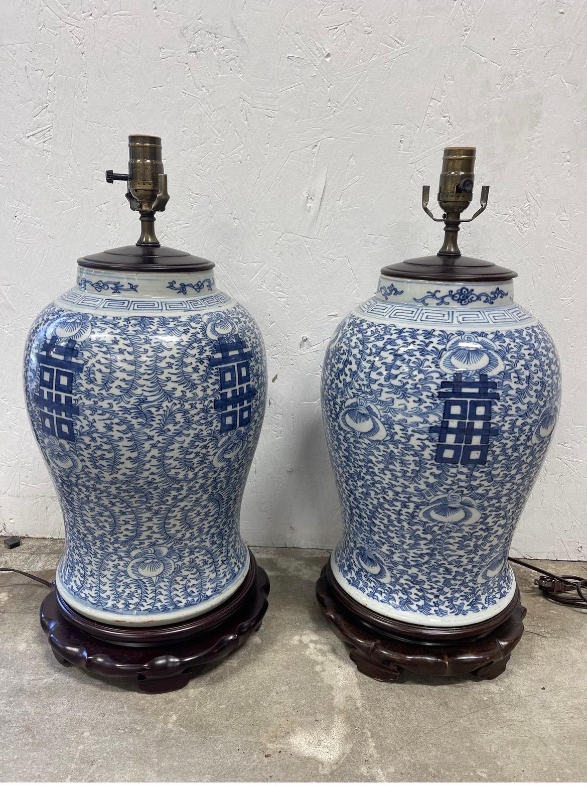 A pair of chinese export style blue and white table lamps with a double happiness symbol to each. Mounted to carved wood base.