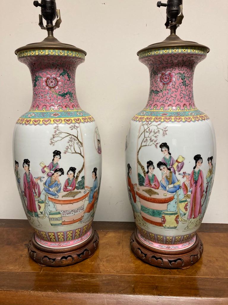 Nice pair of famille rose lamps, finely enameled with court ladies playing mahjong at a table in a garden setting as others look on. Four lines of calligraphy, with seal marks. The neck decorated with stylised flowers and scrolls on a pink ground,