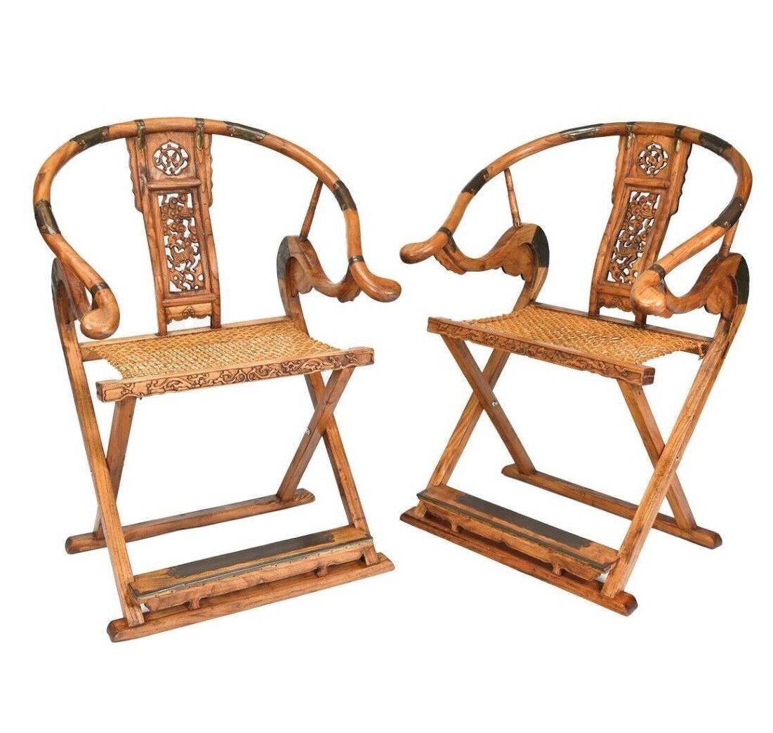 A pair of Chinese solid elmwood horseshoe folding chairs. Each chair constructed with a rounded metal mounted crestrail ending in outswept handrests. The back splat carved with qiling motif and cloud scroll, under a coiled dragon in a ruyi