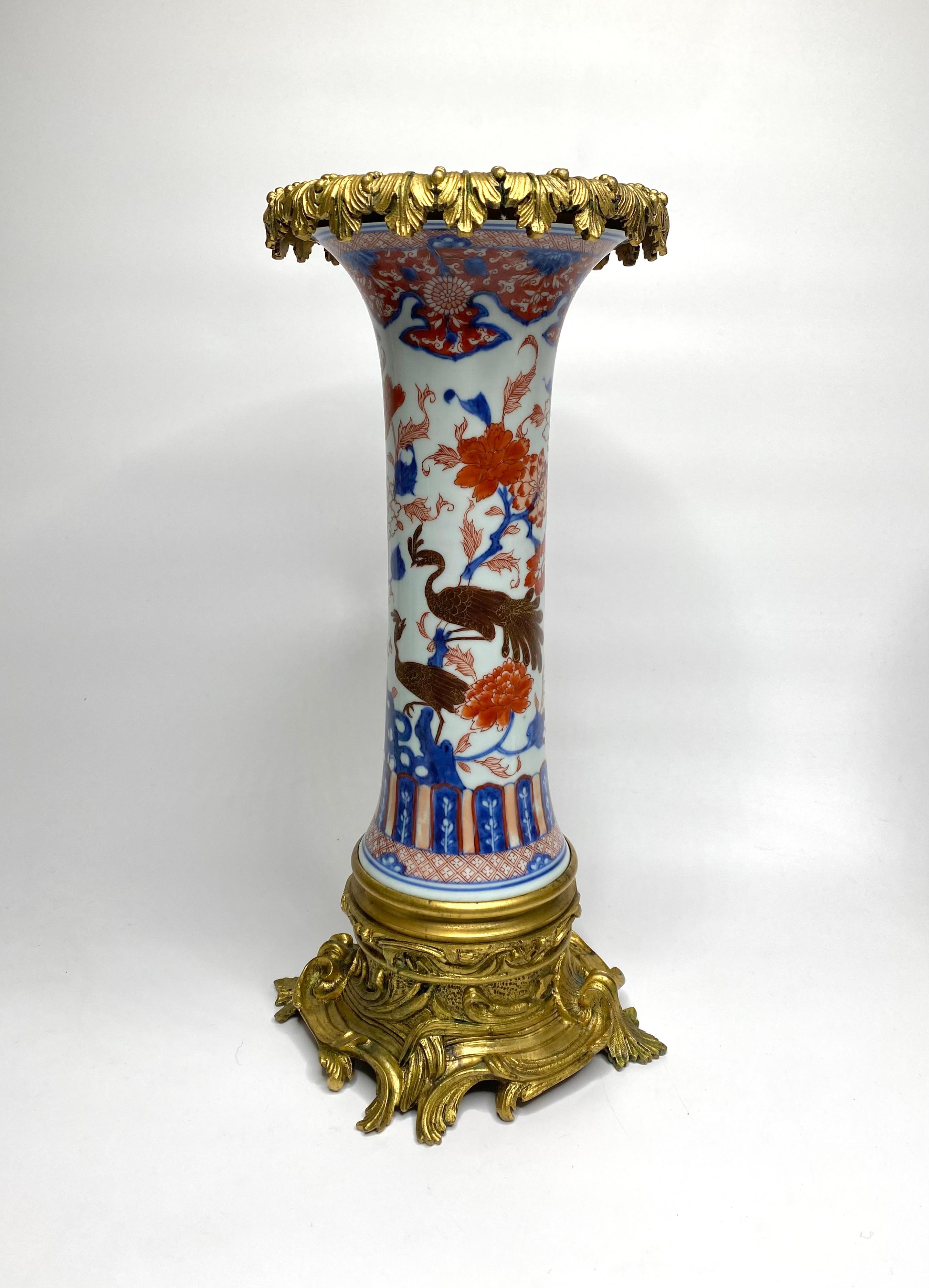 A fine pair of Chinese porcelain vases, c. 1700, Kangxi Period, ormolu mounted. The trumpet shaped vases, hand painted in Imari style, with exotic birds amongst flowering plants, above a continuous lappet and cell net motif. The upper rim painted