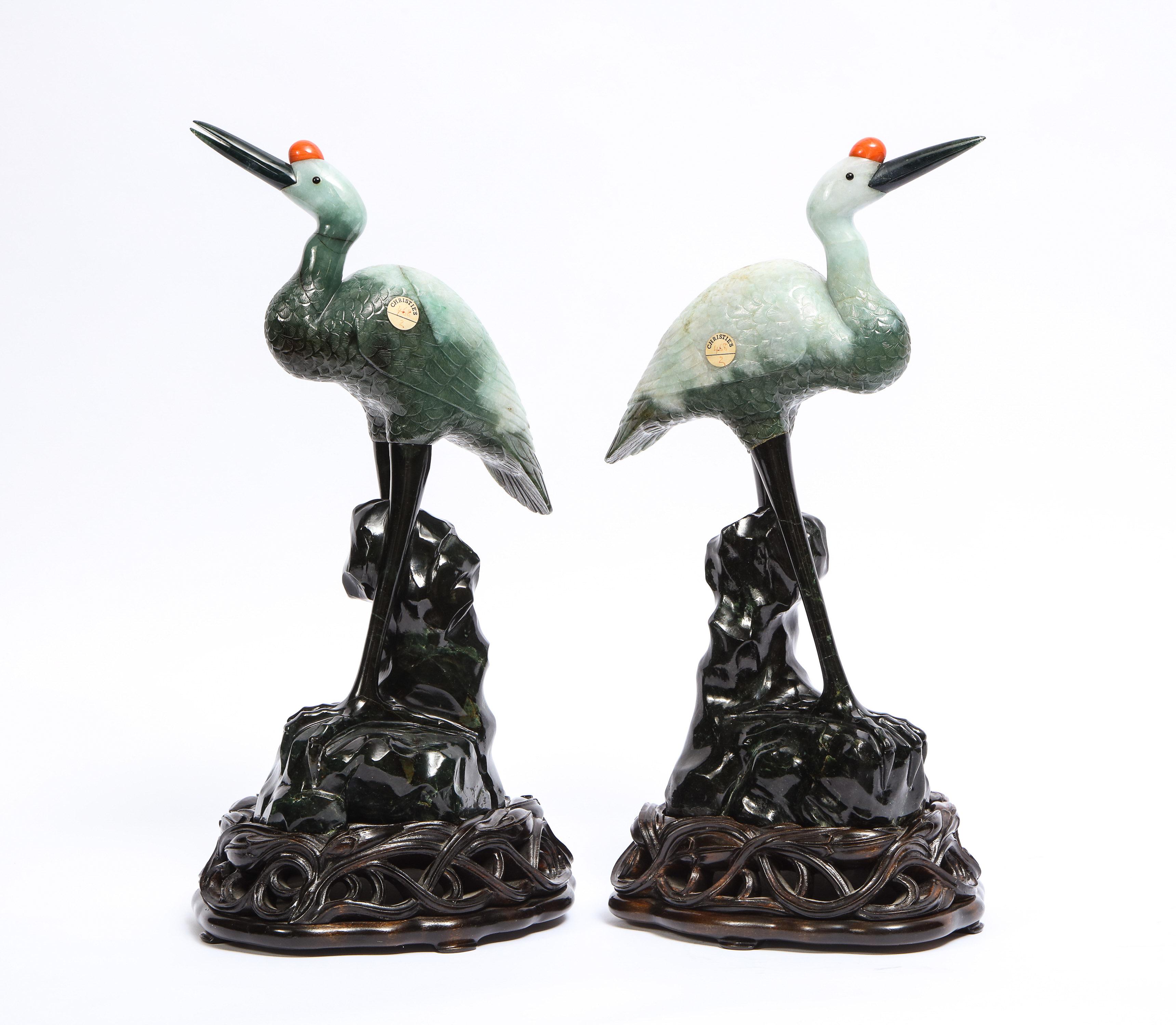 A fabulous pair of Antique Chinese mottled light green jadeite carvings of cranes on hand-carved wood stands. Each of pieced construction the body of mottled light green with an inset beak and red coral crown, supported on spinach jade legs, atop