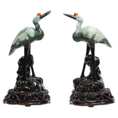 Coppia di sculture cinesi in giadeite verde chiaro screziata, gru su supporti in legno intagliato