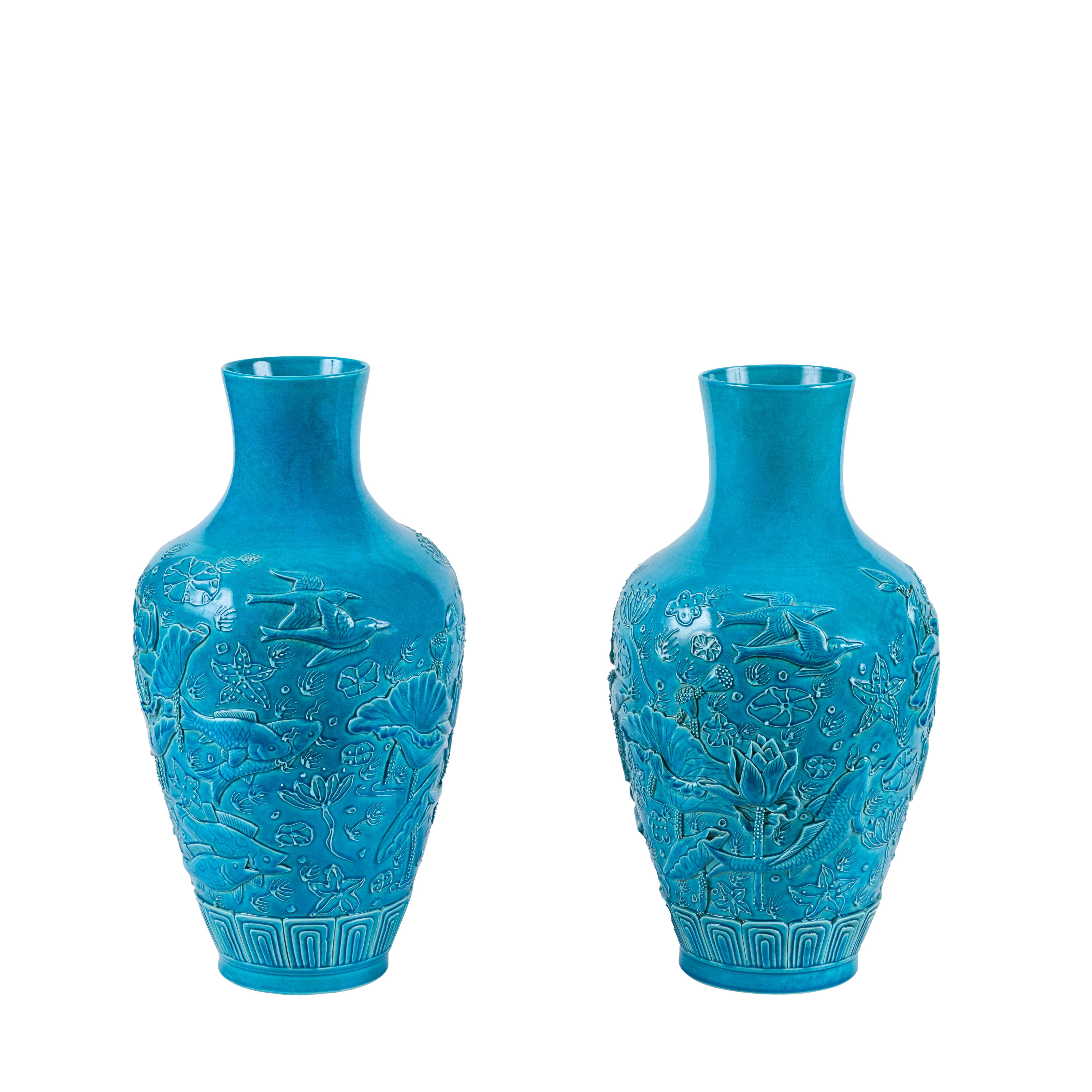 Coppia di vasi in porcellana smaltata turchese con rilievi decorativi che includono koi, fiori di loto e altri temi della cineseria.