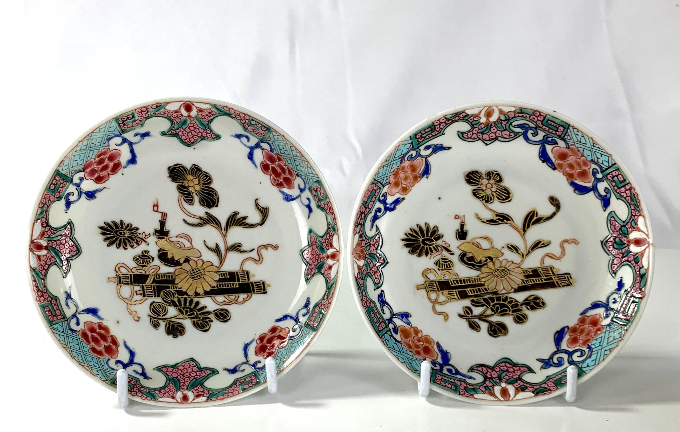 This pair of lovely hand-painted saucers were made in 18th-century China circa 1780.
In the center of each saucer, we see flowers painted in gold and midnight brown.
The fabulous Famille Rose colors of the border catch the eye. 
The combination of