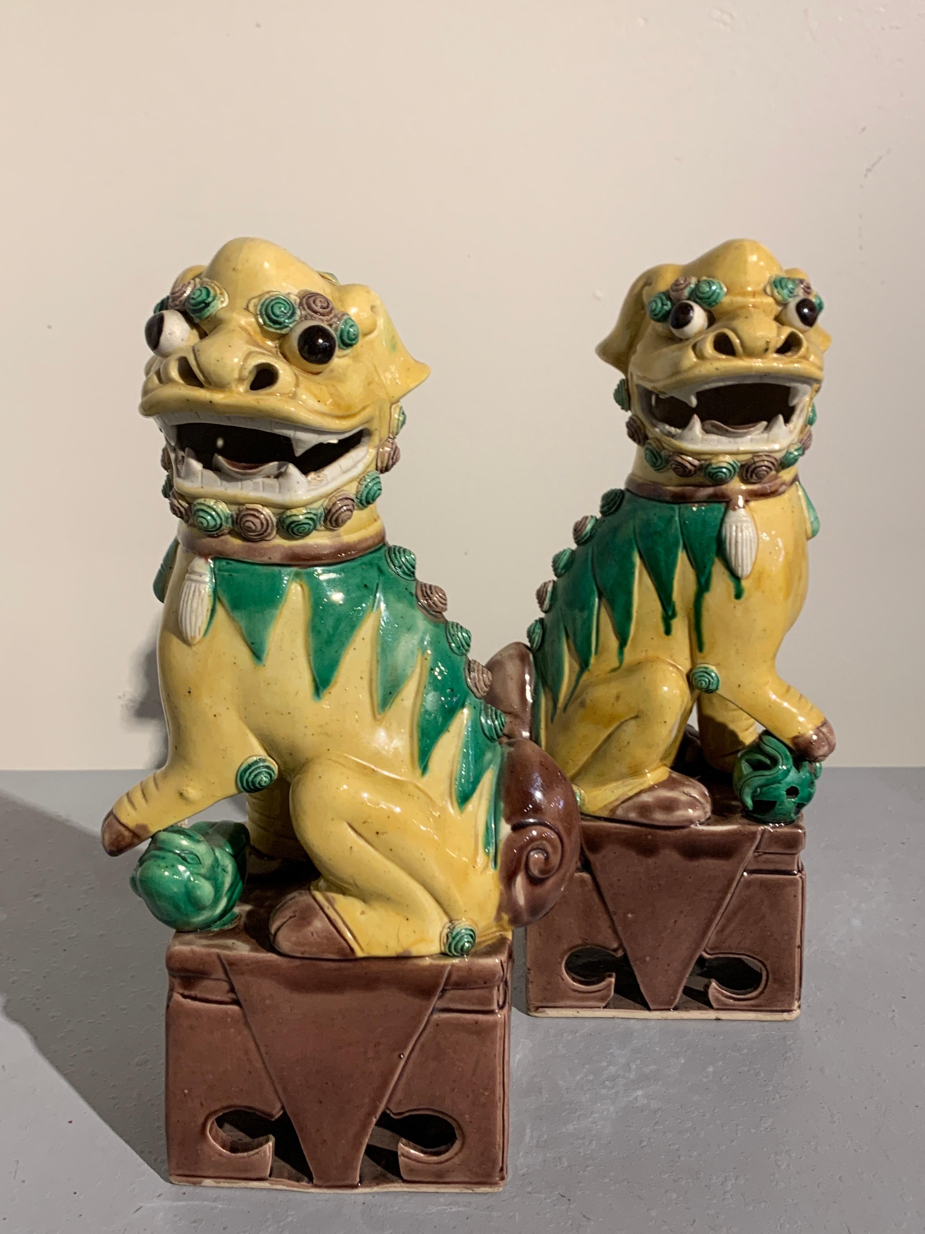 A charming pair of Chinese porcelain foo dogs in yellow, green and brownish purple glazes, Republic Period, circa 1930s. 

Each whimsical foo dog glazed yellow with green and puce highlights, and seated upon a brownish purple glazed plinth. Their