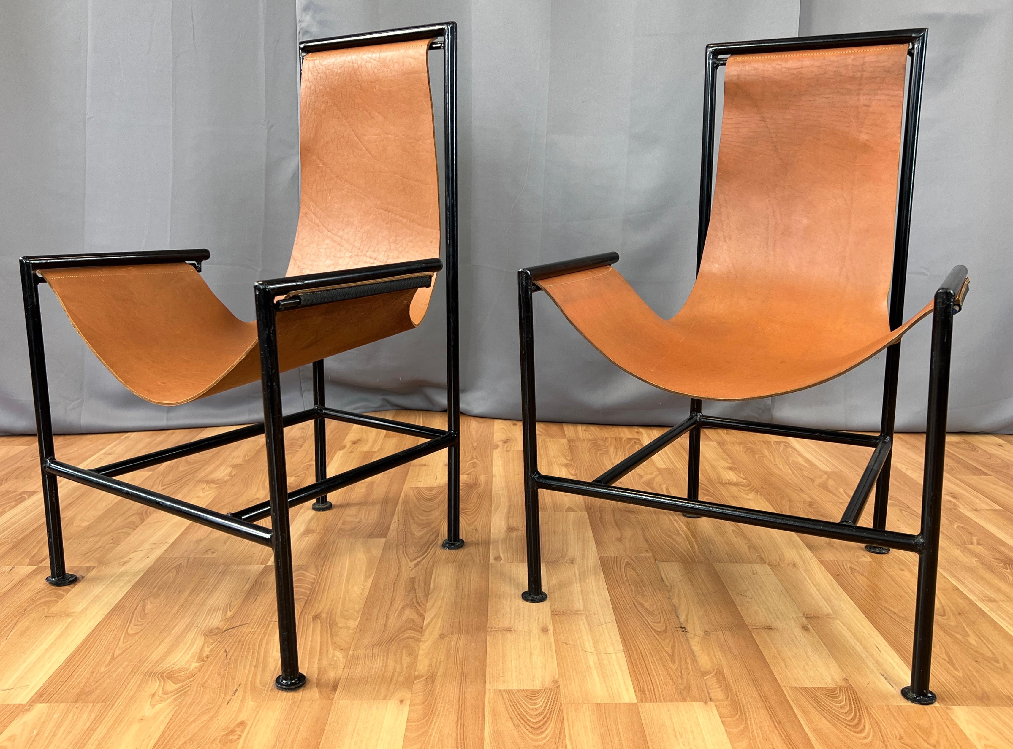 Offered here is a pair T-style sling lounge chairs with a brown leather sling. 
Simple design, black metal frame, with the ends of the leather sling going through a slot. 
Leather at it's end, has fabric tubes, where a metal rod goes through, that
