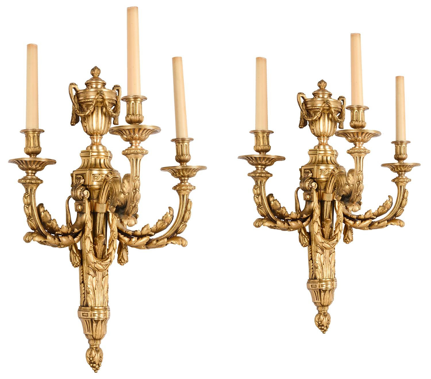 A good quality pair of late 19th century gilded Ormolu three branch wall lights, each with classical two handled urns and scrolling foliate swags, in the Louis XVI style. Measures: 63cm (25