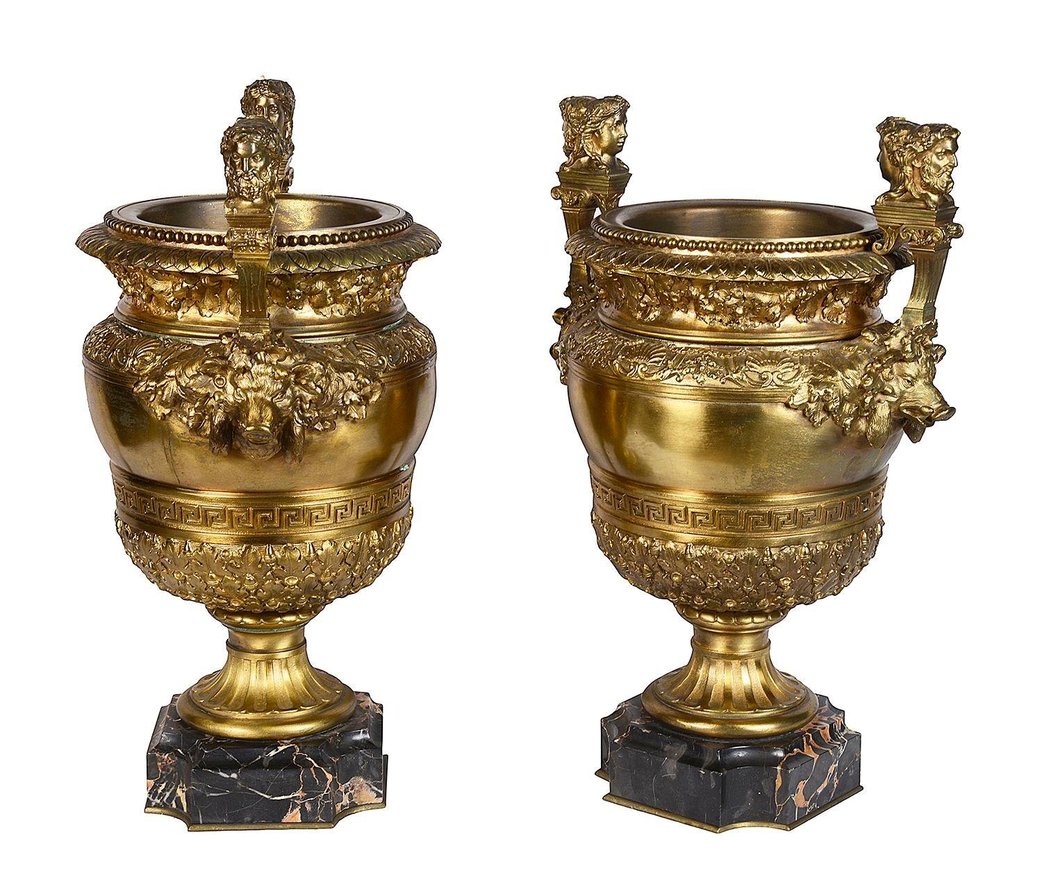 A very impressive pair of Classical 19th Century French gilded ormolu urns.
Each with two-headed Janus finials, the sides with boar's masks and bands of shells, oak leaves and Greek key pattern decoration, raised on pedestal bases and mounted on