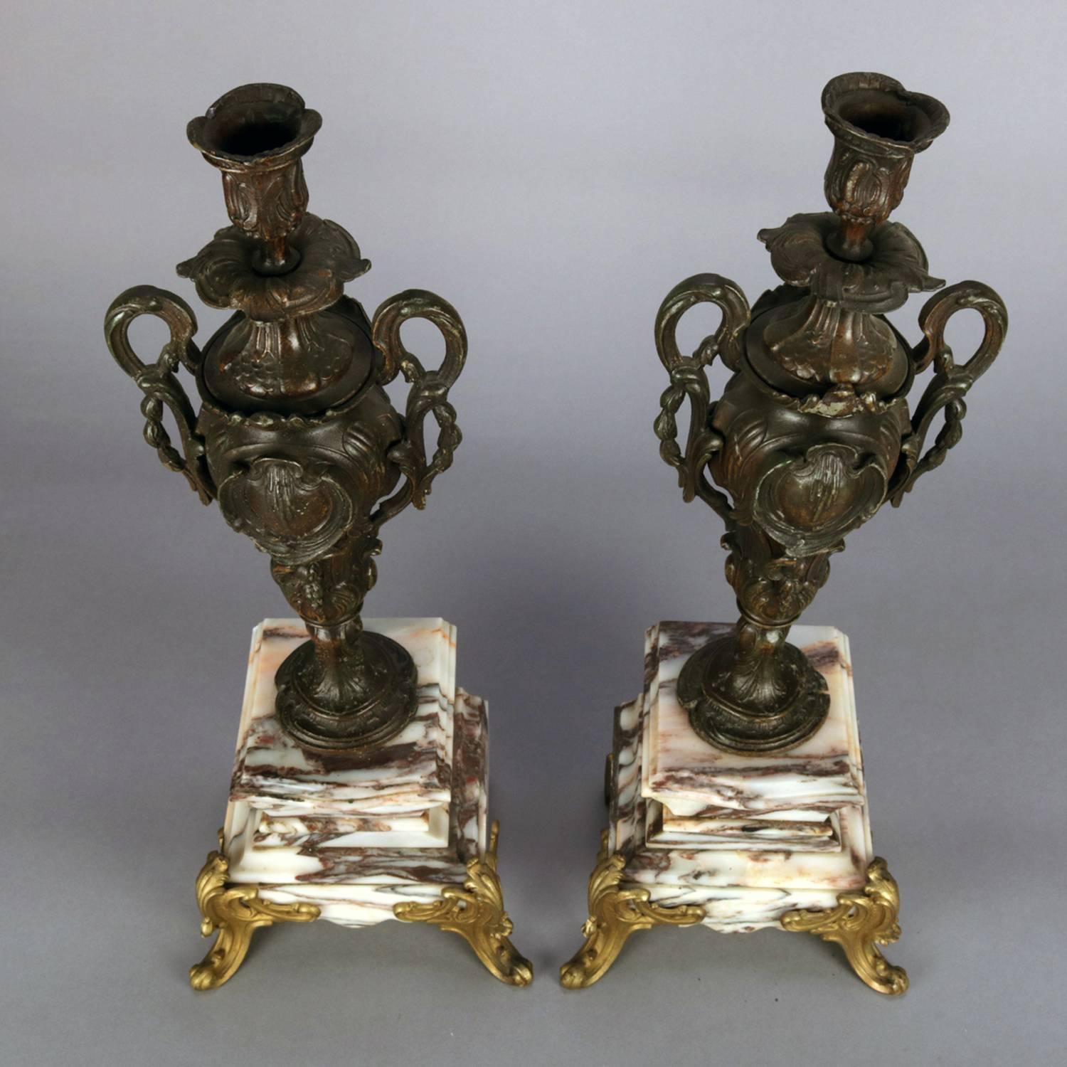 Antique pair of classical candle sticks feature cast bronze double handle urn form with embossed scroll and foliate reserves, seated on deeply variegated marble base with gilt legs, circa 1890.

Measures: 18.5