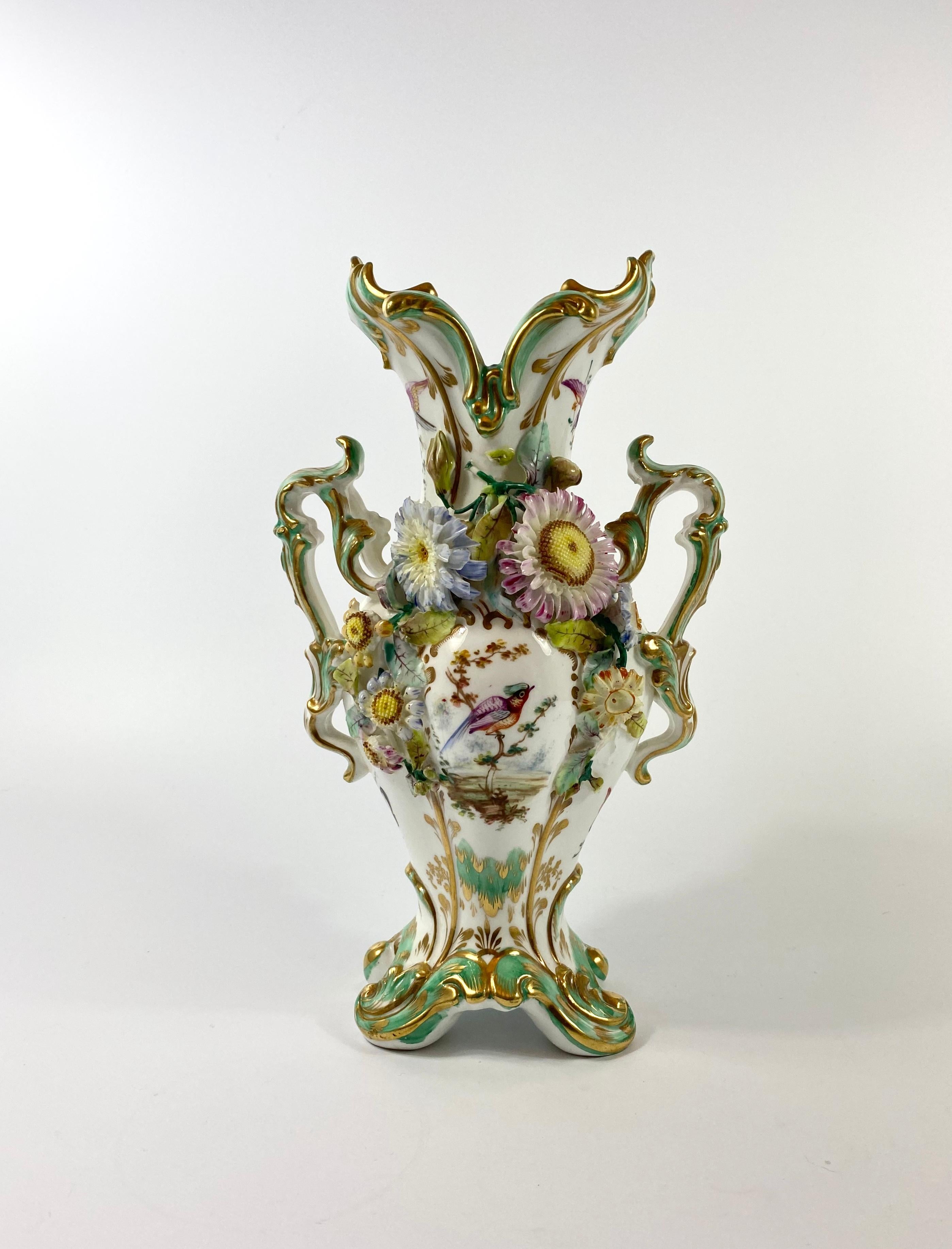 Pair of Coalbrookdale porcelain vases, circa 1830. Both vases beautifully hand painted with studies of birds, within gilt rococo scroll panels. Heavily encrusted with brightly enamelled flowers, having twin scroll handles and set upon four scroll