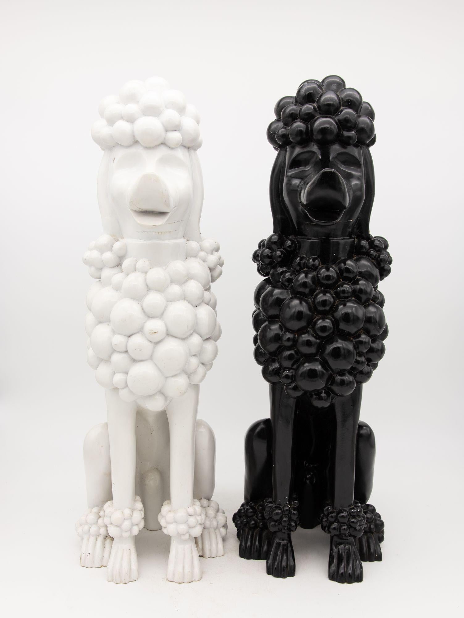 A delightful duo of composite lifesize Poodles, one ebony and one snowy white! Likely advertising models, these enchanting sculptures radiate charm and joy with their endearing and cheerful expressions. Crafted with exquisite attention to detail,