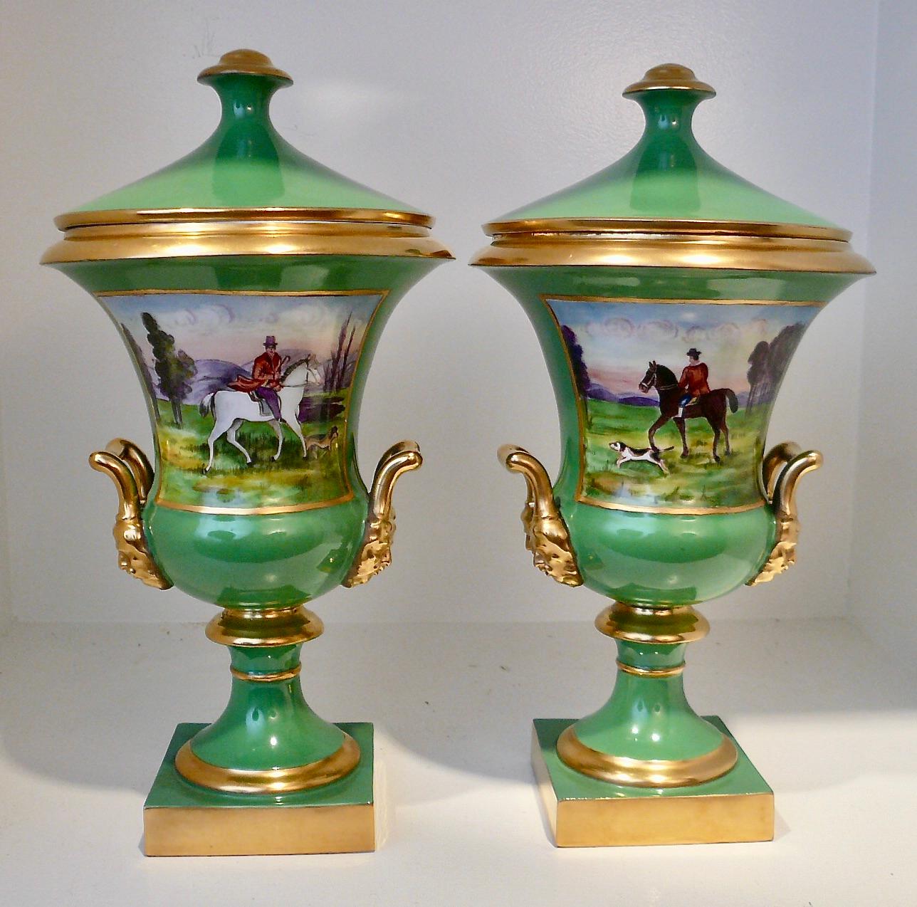 The handsome pair of apple green hand painted porcelain urns and covers feature hunting scenes on one side, and floral bouquets on the other.