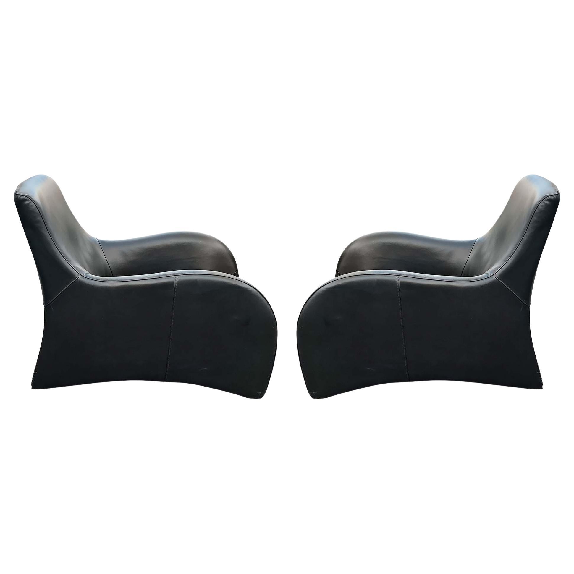 Une paire de fauteuils de salon ou fauteuils club aux courbes très prononcées, en cuir noir surpiqué, reposant sur des pieds discrets en métal chromé. Ces chaises ressemblent beaucoup à la version iconique rendue célèbre par le designer néerlandais
