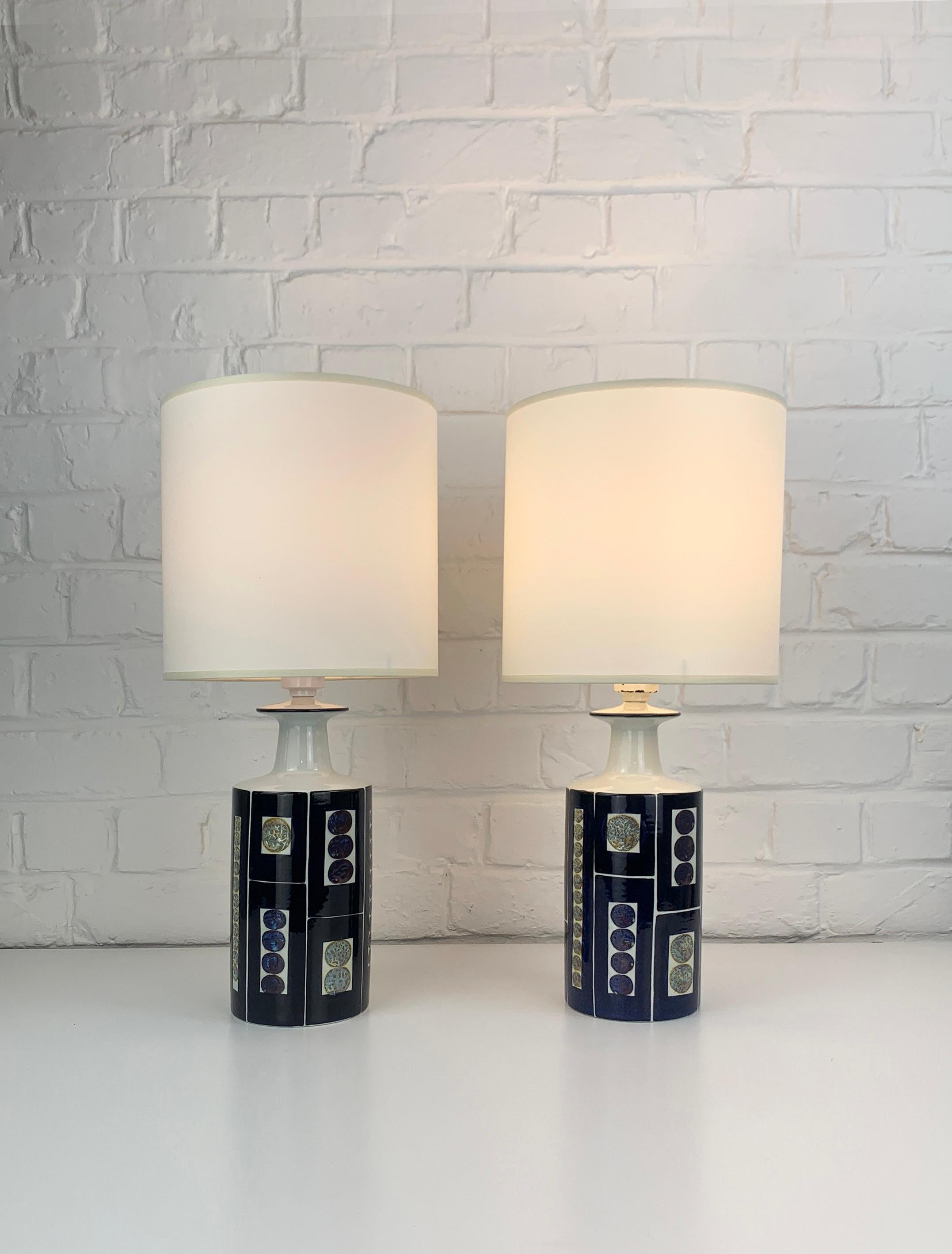 Pair table lamps from the late 1960s or early 1970s. These lamps have been manufactured by Royal Copenhagen and sold by Fog & Mørup, Denmark. 

Impressive bold graphic design by Inge-Lise Koefoed, featuring a decor in dark blue with greyish / beige