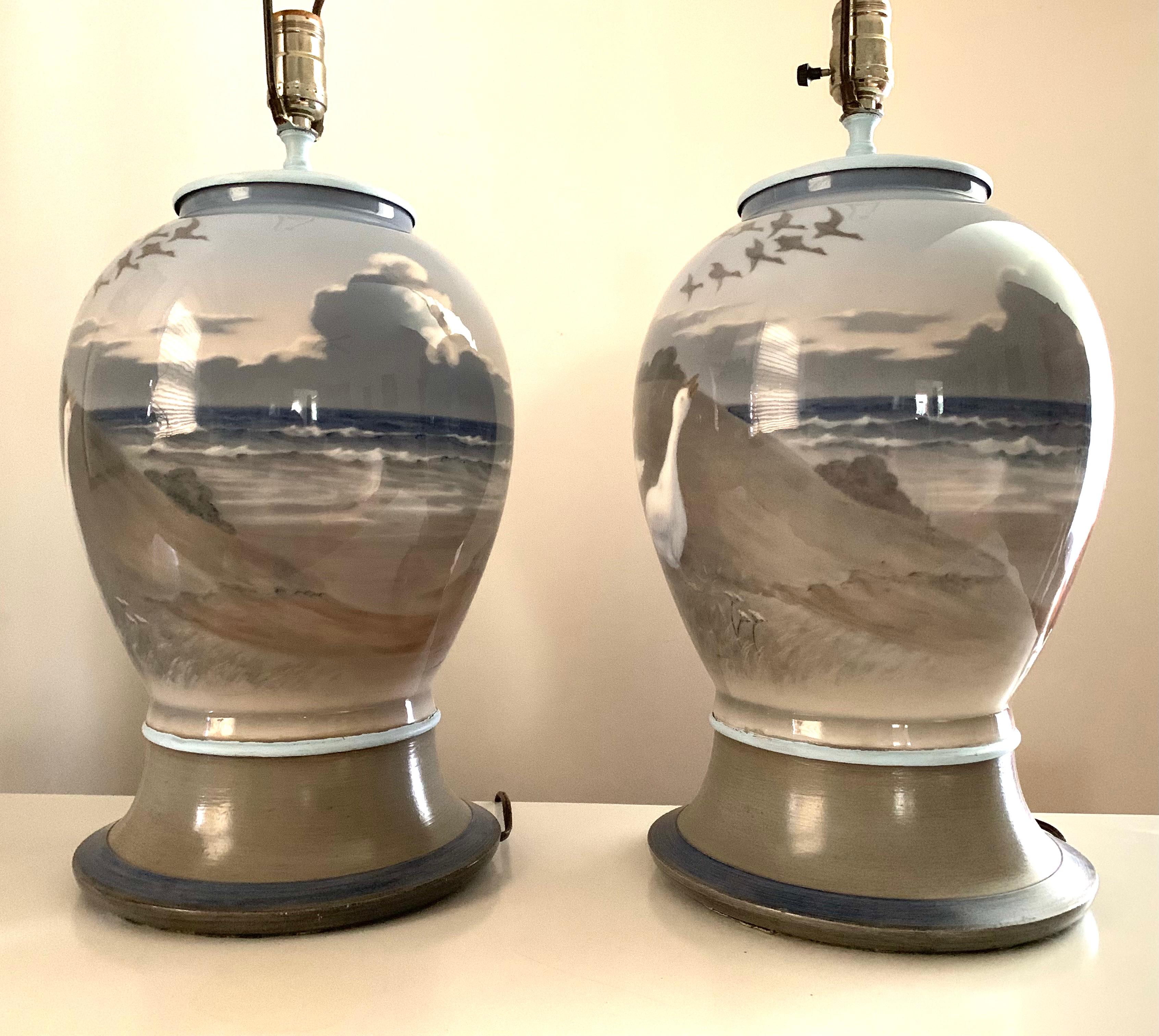Silvery grey and blue tones create a magical beach sea shore setting depicted in these hand painted custom mounted lamps. The porcelain vessels are Royal Copenhagen, circa 1920 with custom made hand painted complementary wooden bases. Large,