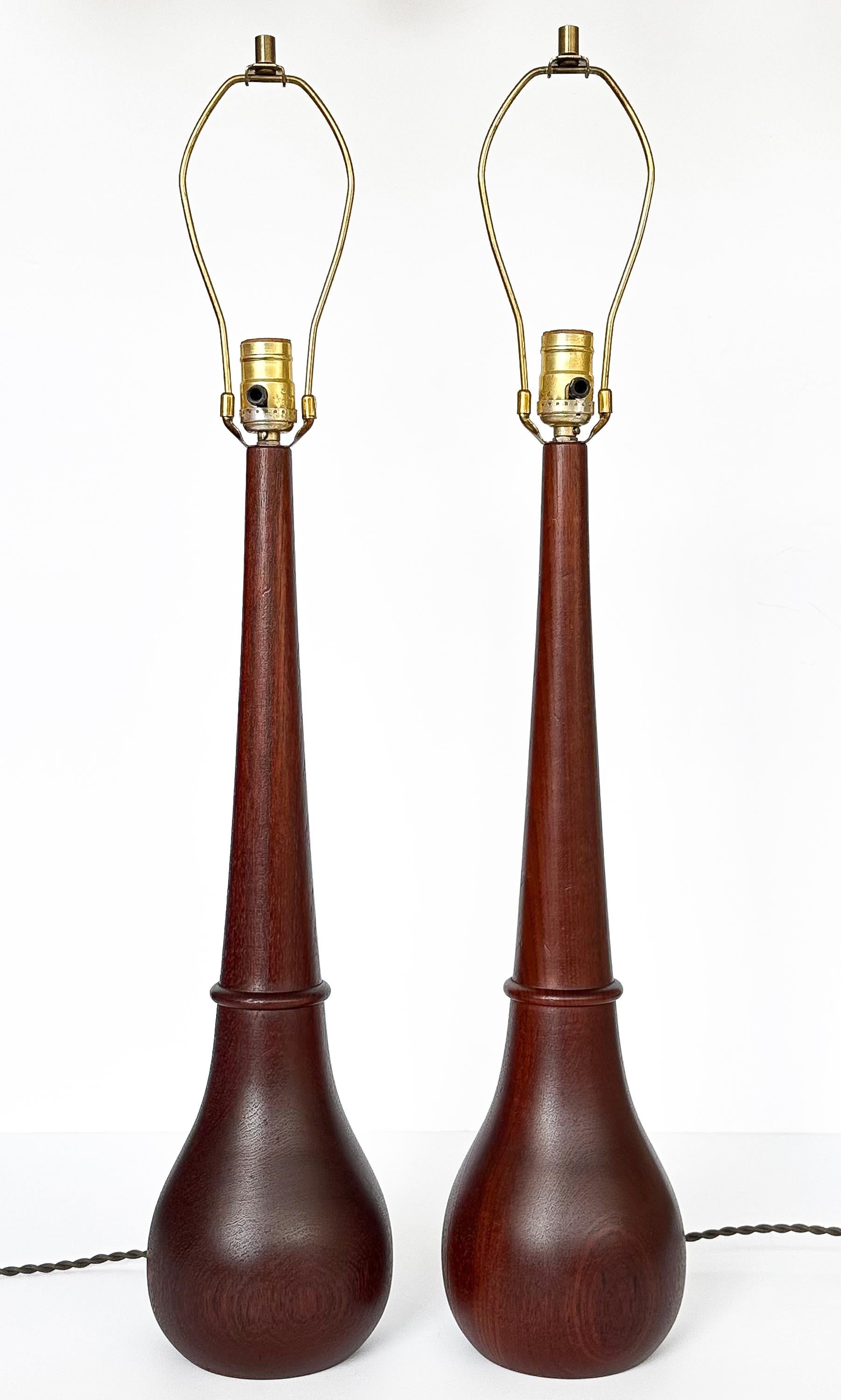 A splendid pair of uncommon sculptural Danish solid teak table lamps, Denmark circa 1950s. Each lamp, with its bulbous bottle-form, tells a tale of meticulous crafting. The choice of solid teak wood, enriched with a lustrous walnut stain, speaks of