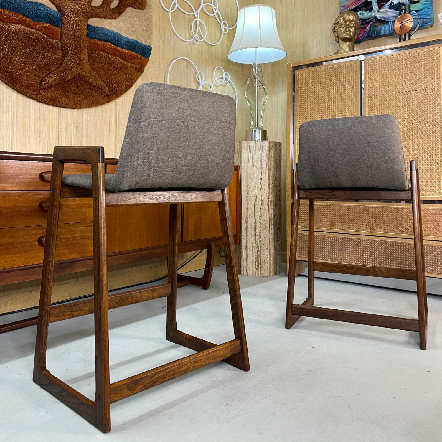 Pair of restored Danish teak counter height barstools in new taupe upholstery. These stools date from 1980s. They were originally purchased from Copenhagen Imports Scandinavian Modern furniture store in Sarasota, Florida. The original owner kept