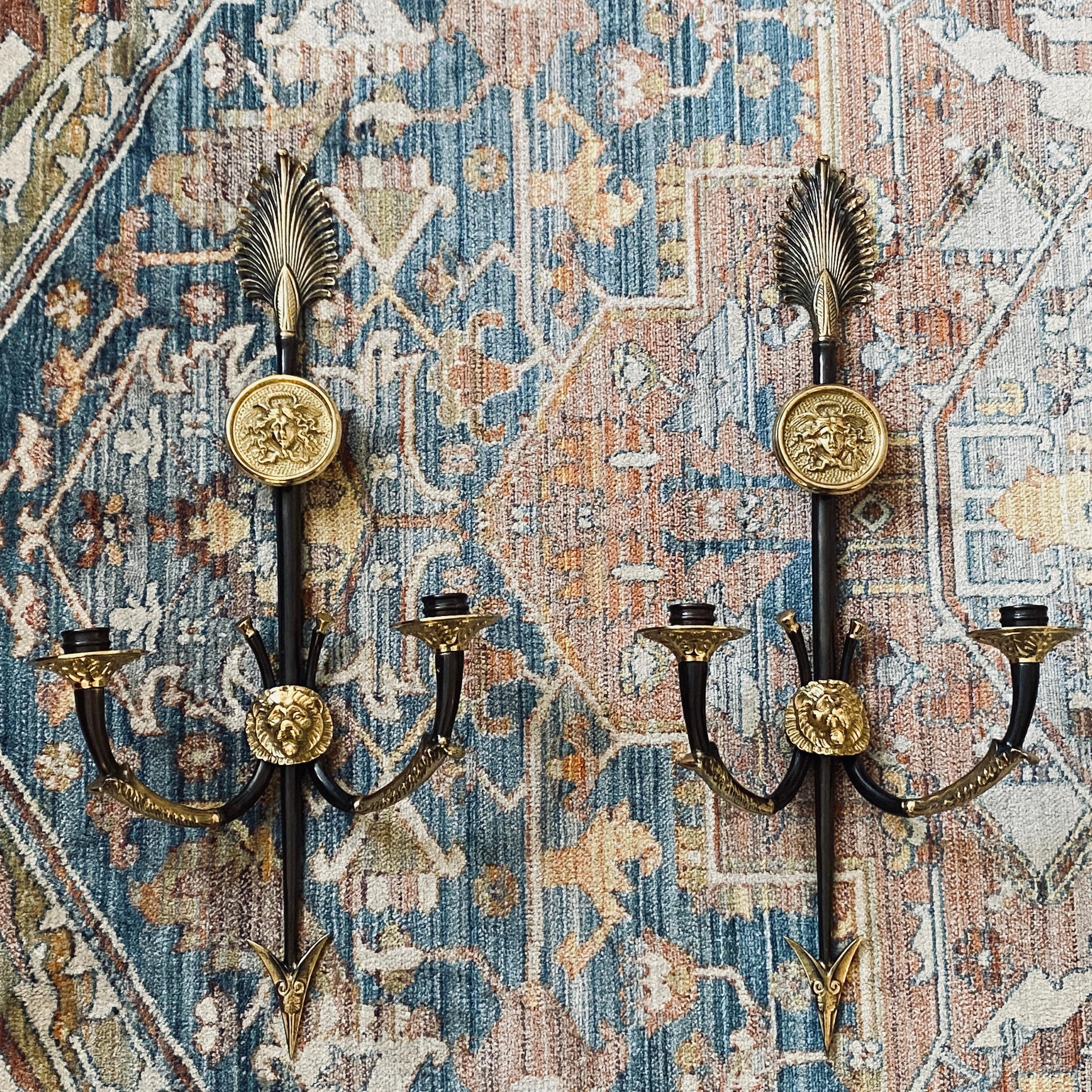 Pair of heavy solid brass finely detailed two arm candle sconces handmade by Decorative Crafts Inc. featuring vertical feathered arrow or spear with a lions head holding the decorative arms.