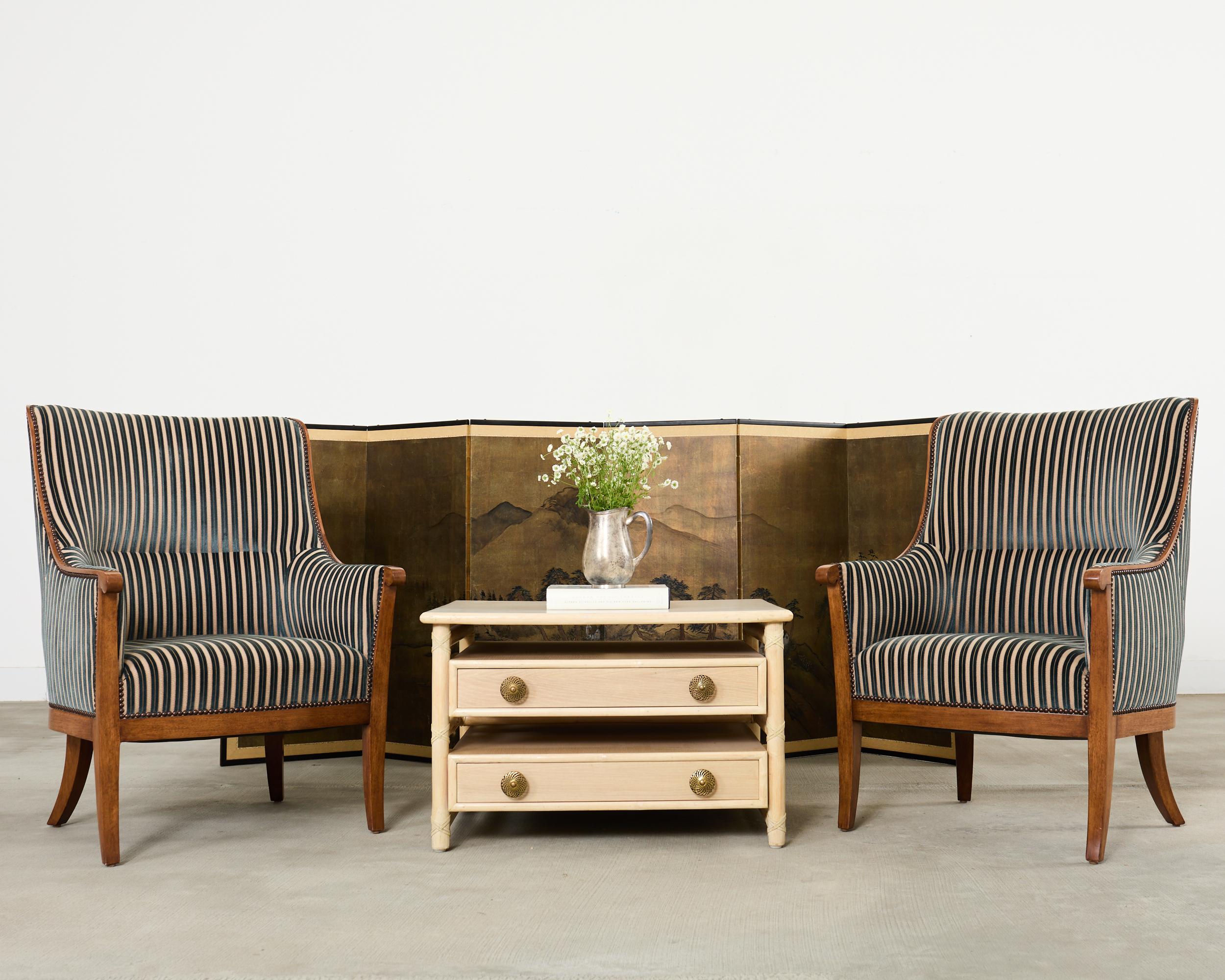 Opulent pair of regency style armchairs or library chairs crafted from fine walnut by Dessin Fournir. The Alexandria chairs feature a gracefully curved barrel back form with an exposed solid wood frame. The walnut frames are upholstered with a