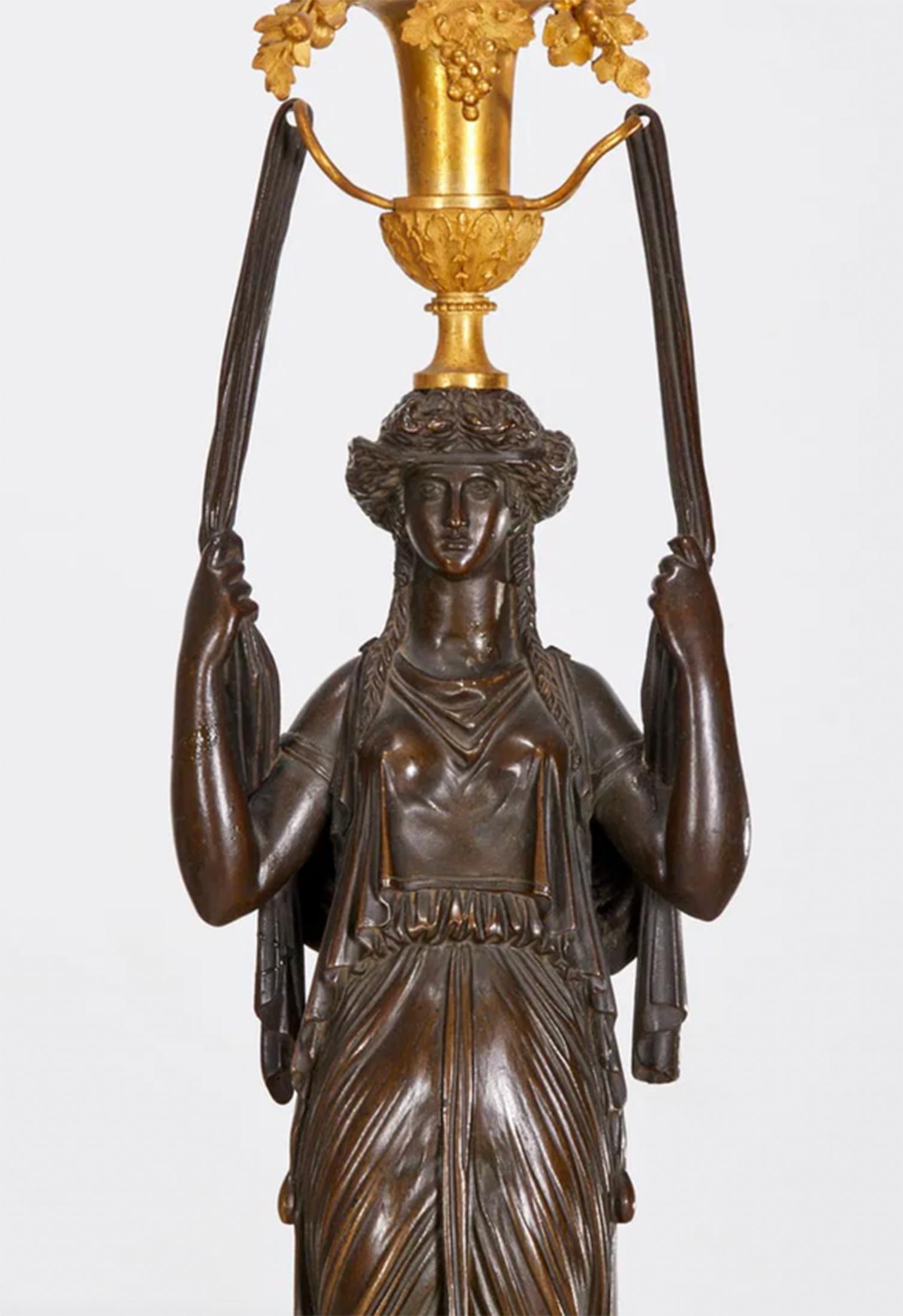 Paire de candélabres en bronze et bronze doré d'époque Directoire, avec des figures néoclassiques en bronze patiné foncé portant des robes drapées, tenant chacune une urne en bronze doré, et reposant sur des piédestaux en marbre blanc avec des