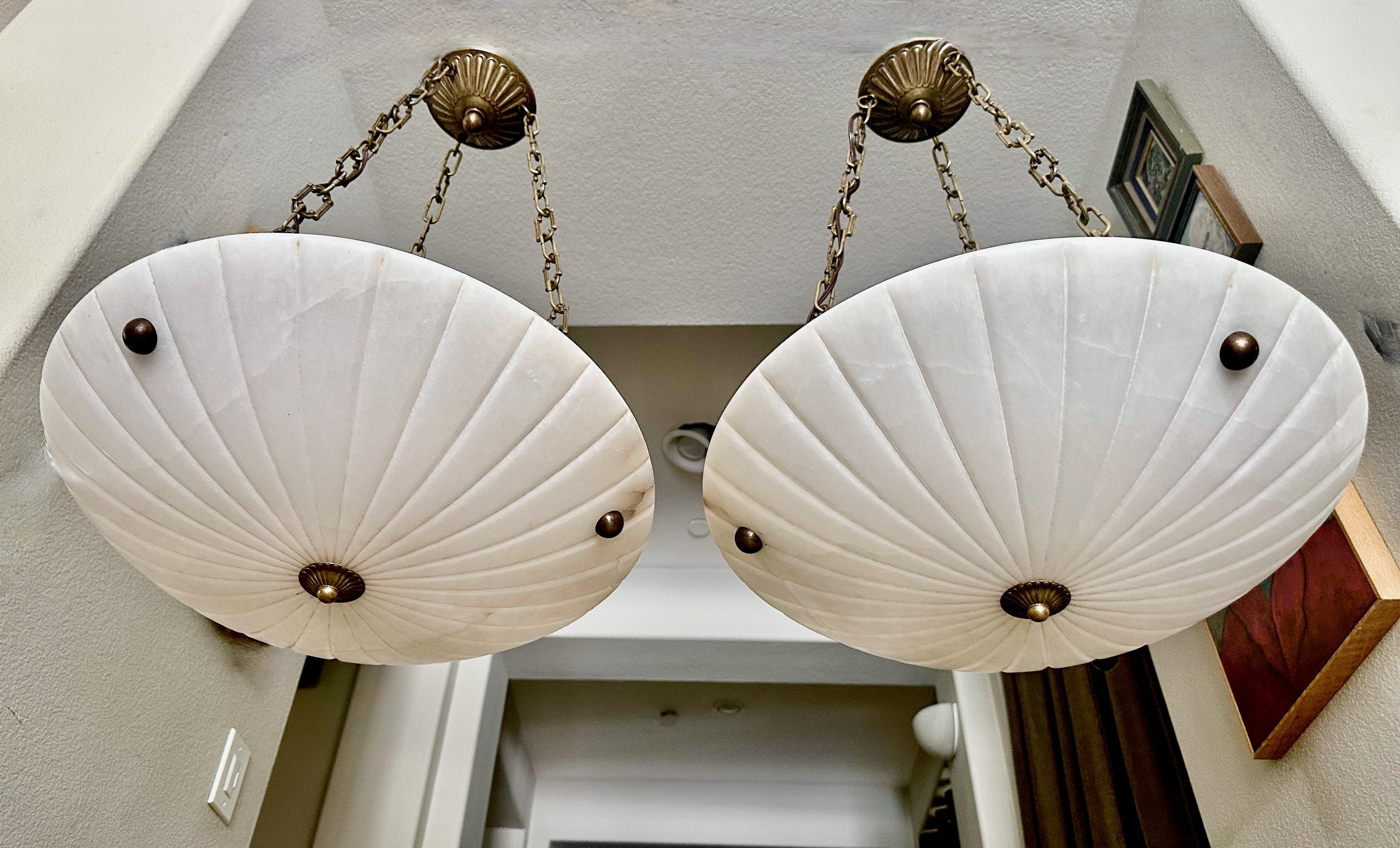 Paire de lampes suspendues en albâtre de style Directoire avec ferrures en laiton vieilli (antiqued). L'éclairage intérieur utilise 3 ampoules de 60 watts à culot intermédiaire (LED recommandées). Câblage récemment effectué. 
