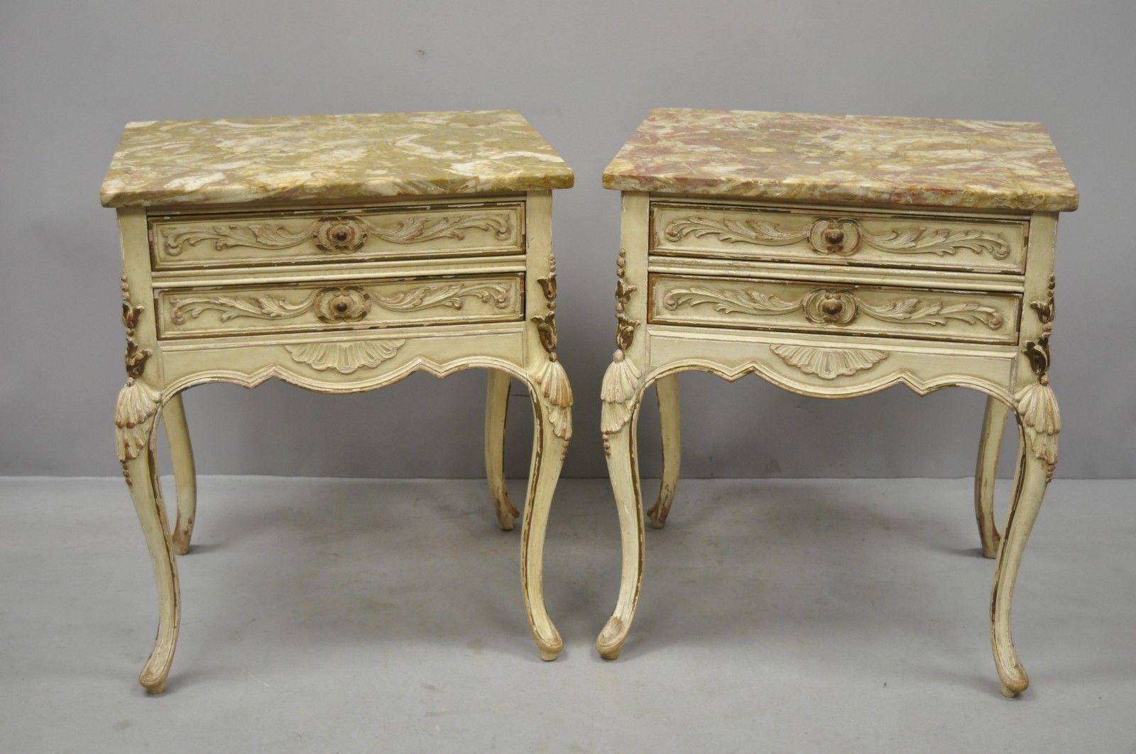 Pair of distress painted French Louis XV marble-top end tables by Danby. Items feature carved wood shells on sides, marble tops, distressed or flaked cream painted finish, finished back, 2 dovetailed drawers, cabriole legs, quality American