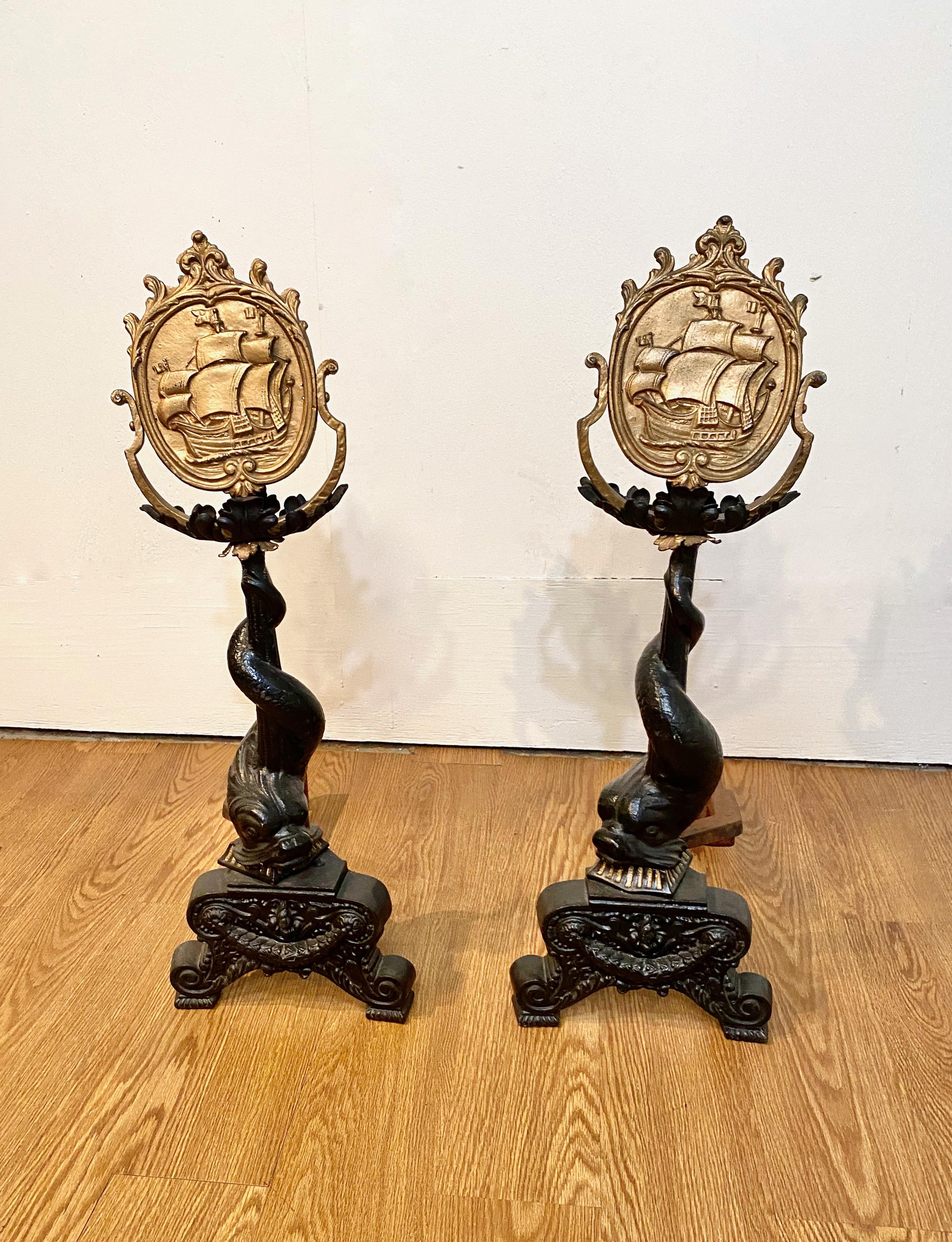 This is an exceptional pair of large c. 1850 cast iron andirons. The andiron shaft is composed of a mythological dolphin on a classical plinth surmounted by a medallion encircling a 18th century sailing ship. All elements of the andirons are in very