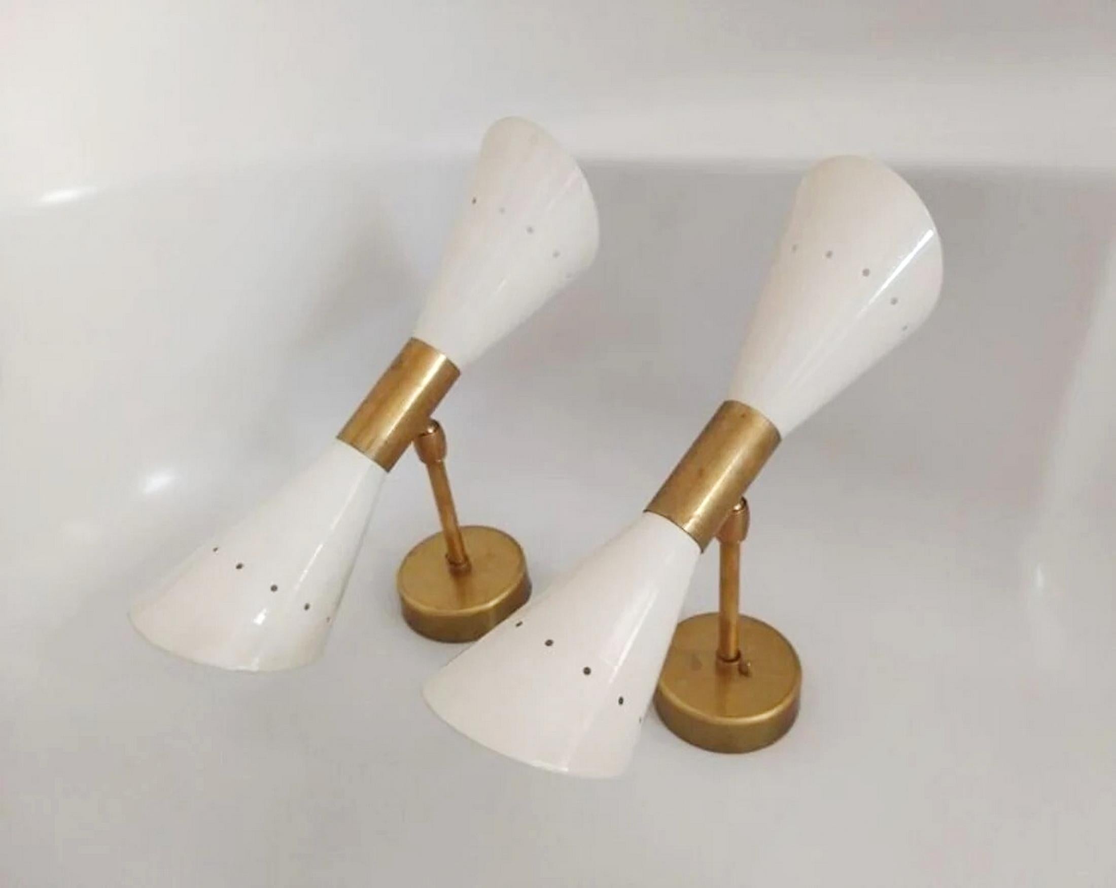 Una coppia scultorea di lampade da parete di metà secolo, caratterizzata da un raffinato gioco di ottone lucido o patinato e metallo laccato avorio. Ogni applique è dotata di un paralume a doppio cono e di due sorgenti luminose che offrono