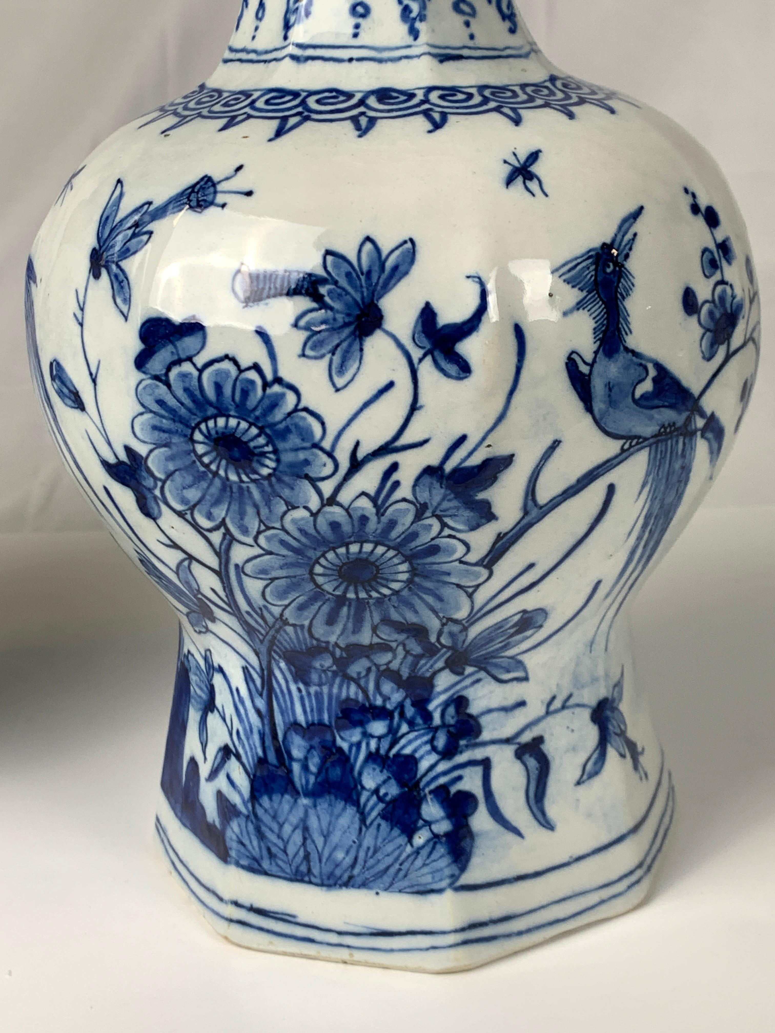 We are pleased to offer this exquisite pair of blue and white Dutch Delft vases hand-painted in shades of cobalt blue with a scene of songbirds on a rocky outcropping surrounded by flowering trees, butterflies, and a garden fence. The design is