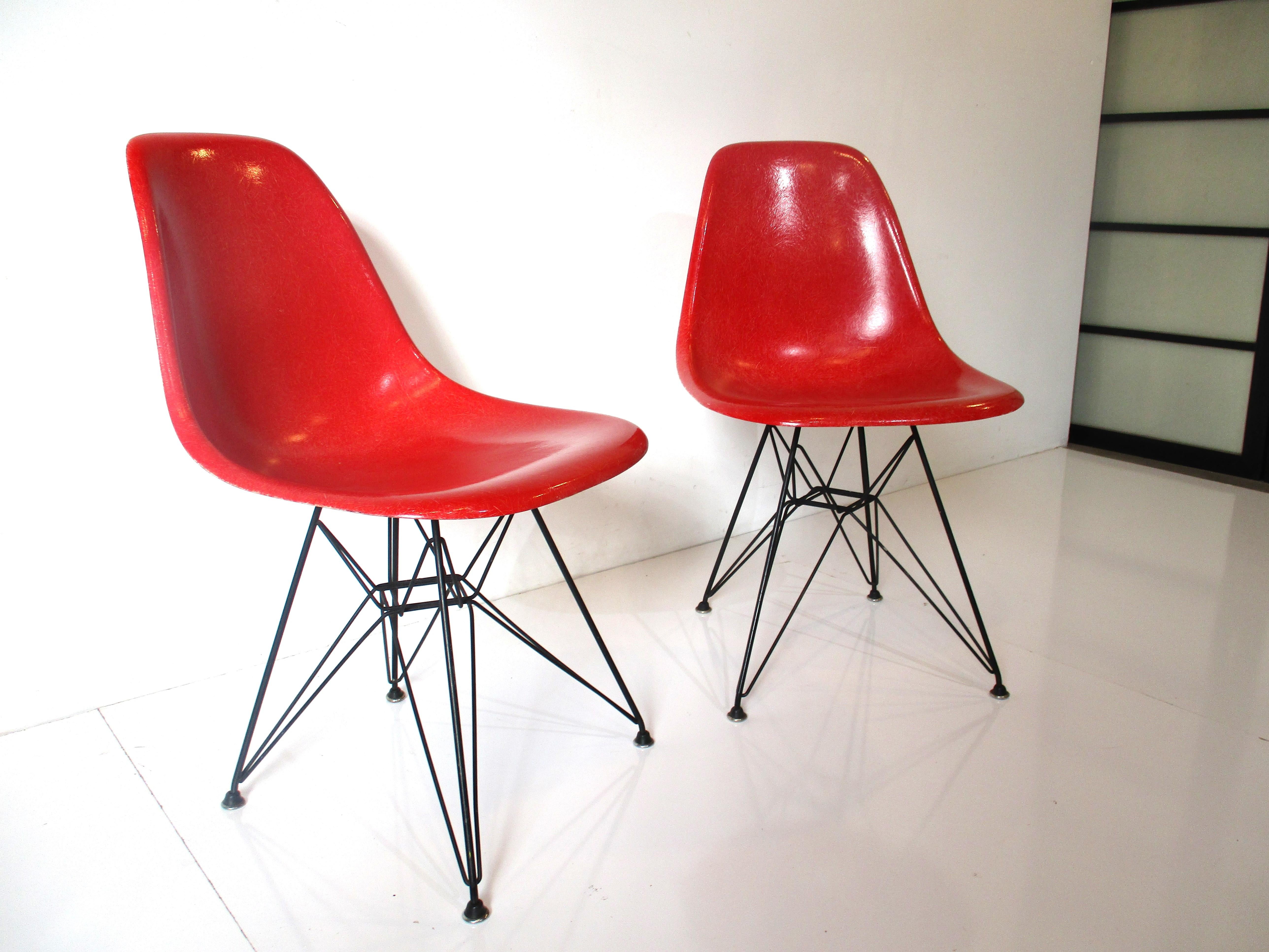 A pair of red molded fiberglass side shell or scoop chairs with sculptural satin black wire metal bases with rubber and metal foot pads. Called the Eiffel tower chairs because of the wire base structure design, manufactured by the Herman Miller