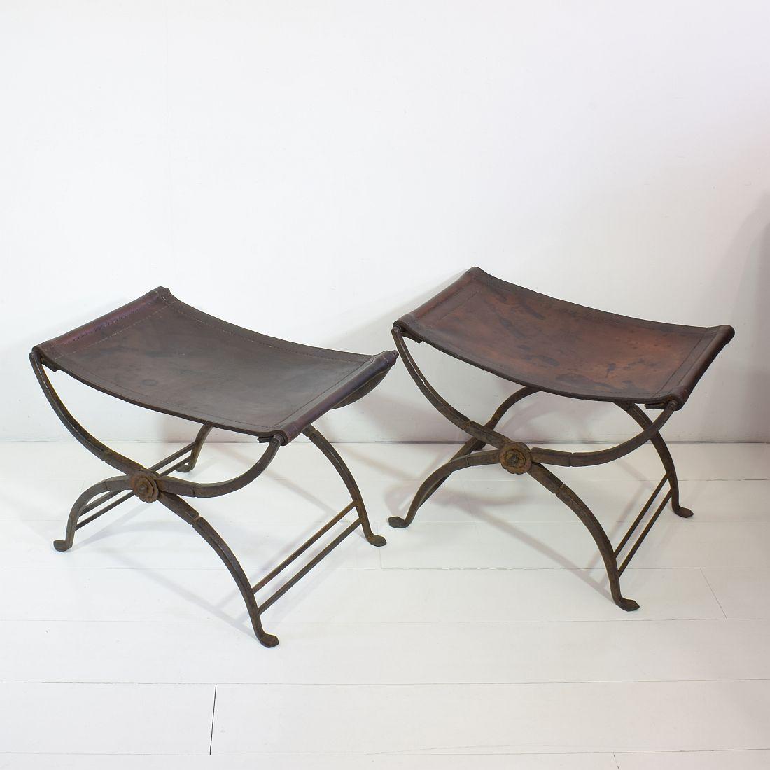 A wonderful and very rare pair of early 19th century Italian wrought iron folding Curule stools with a handstitched saddle leather seat and decorative floral rosettes on both sides where the legs cross. Curule seats were designed by early Romans and