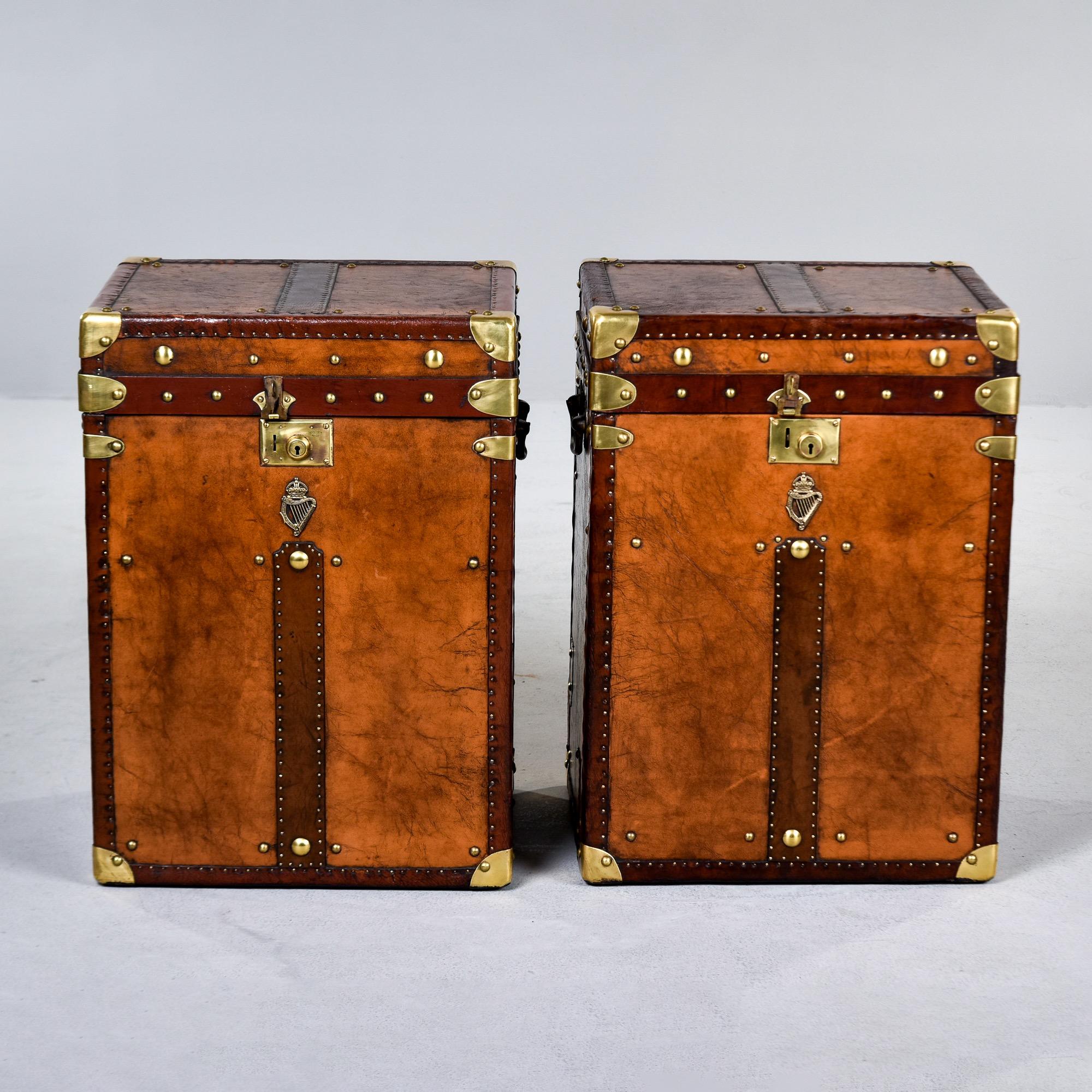 Circa 1920s pair of leather and brass covered trunks found in England. Both trunks have been fully restored with patched leather, new blue velour fabric interior, polished brass hardware and brass regimental emblems. These make great end or side