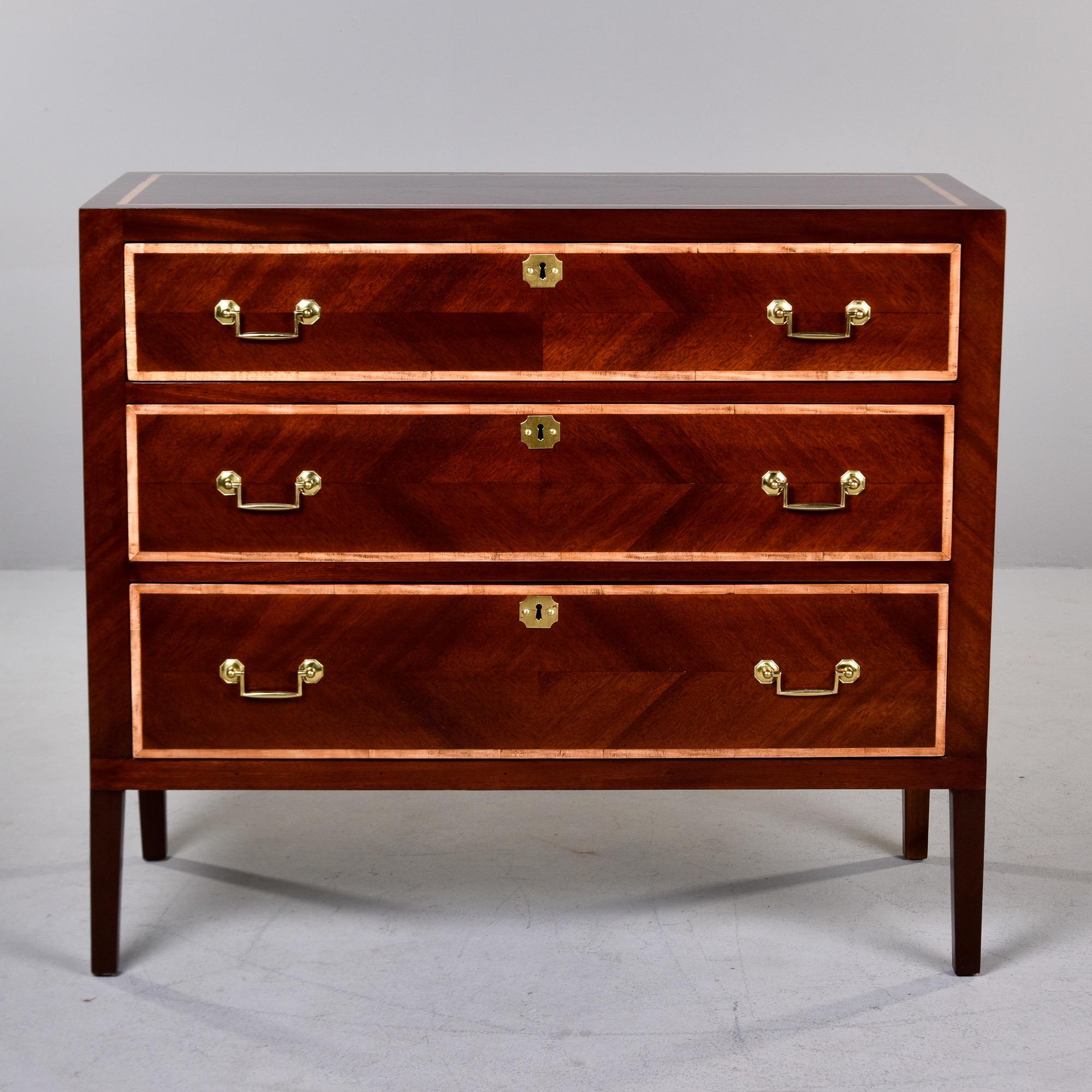 Found in England, this pair of three drawer chests dates from approximately 1900. Chests feature dark walnut veneer arranged in a decorative pattern with contrasting light maple borders on tops and drawer fronts. Brass drawer pulls and escutcheons.