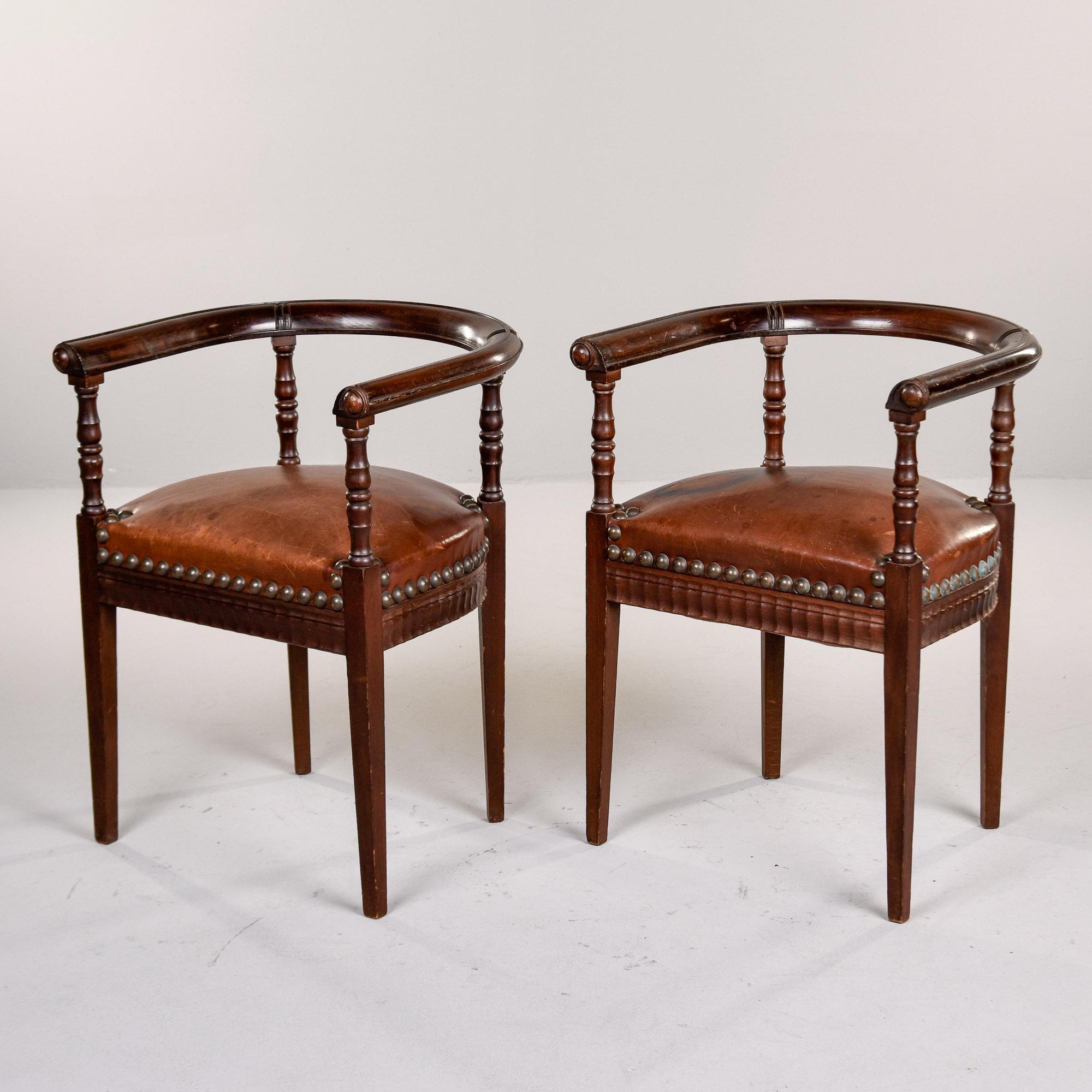 Trouvée en Angleterre, cette paire de chaises de capitaine en acajou et en cuir date du début des années 1900. Les cadres en acajou ont des pieds droits et effilés avec des détails tournés sur les supports d'accoudoir et de dossier. Dossiers