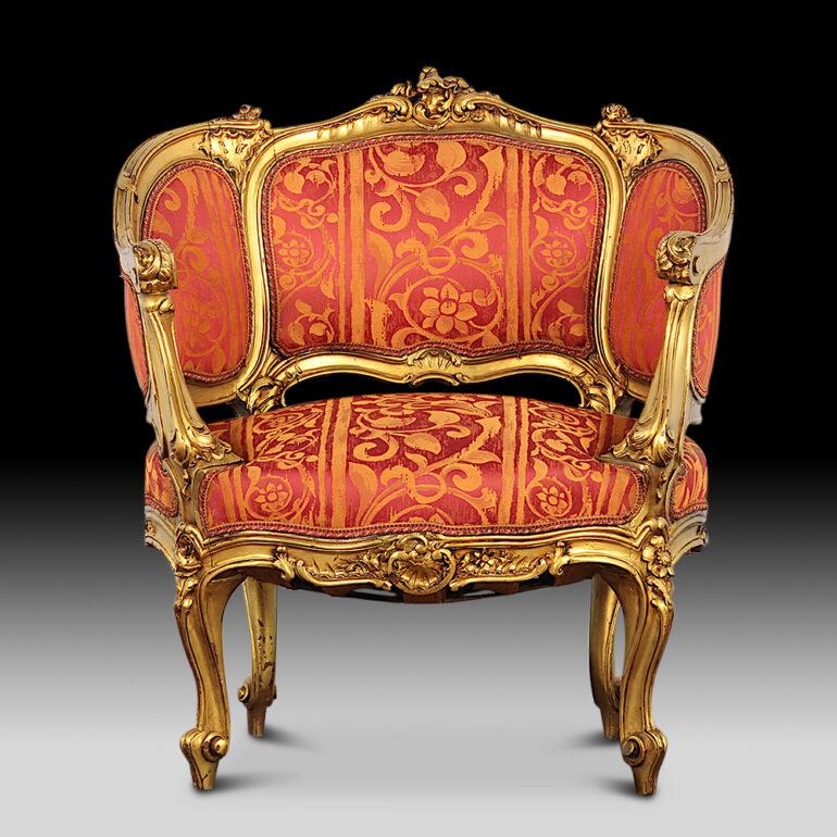 An pair of early 20th century French-made carved and gilt Louis XV style ‘canape’ armchairs, the frames profusely embellished with carved foliage, shells, scrolls etc.